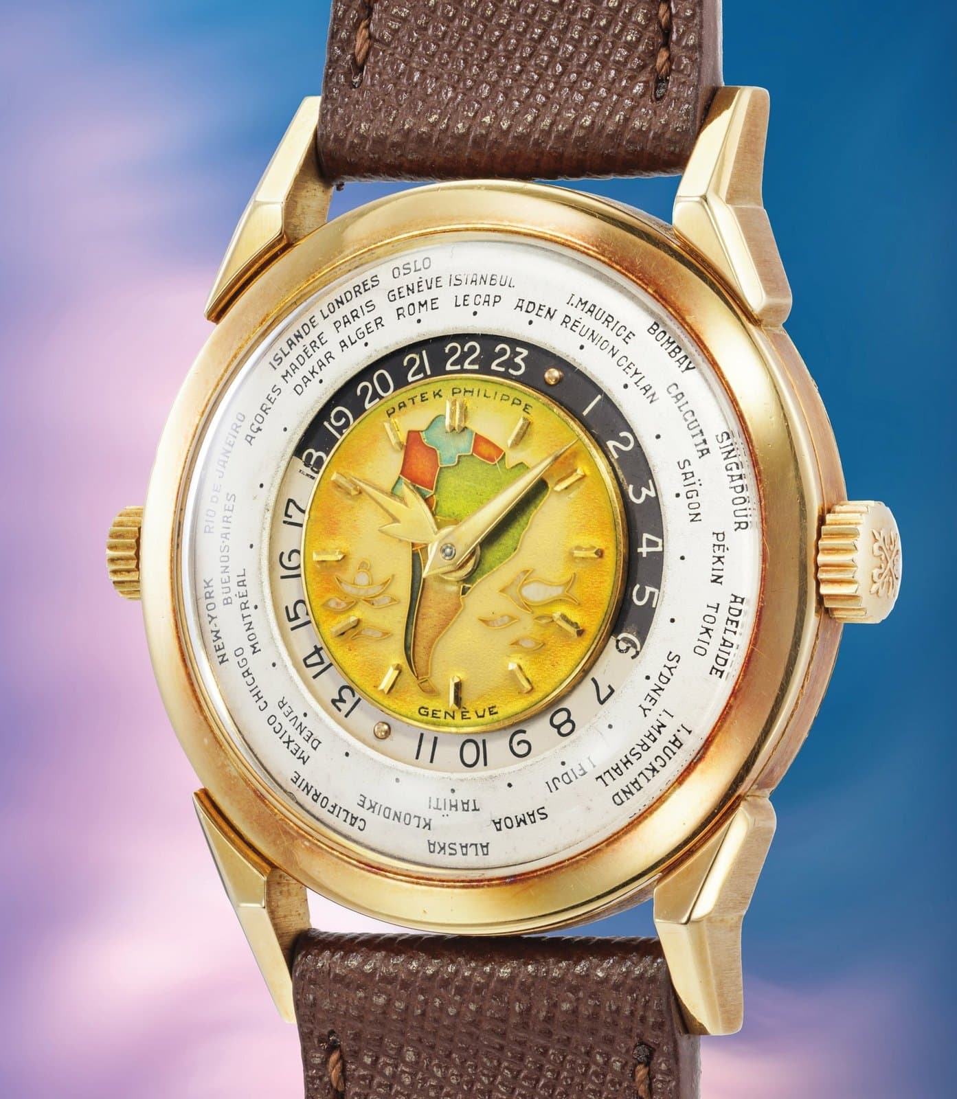 Patek Philippe reference 2523 'Doppia Corona Policromo' in 18k yellow gold, 36mm two-crown world-time wristwatch from 1953, with cloisonné enamel dial depicting the map of South America in green, yellow and orange tones, applied yellow gold hour markers, gold dauphine hands, outer rotating city ring with names including New York, Paris, Geneva and Tokyo, on a brown leather strap with yellow gold pin buckle