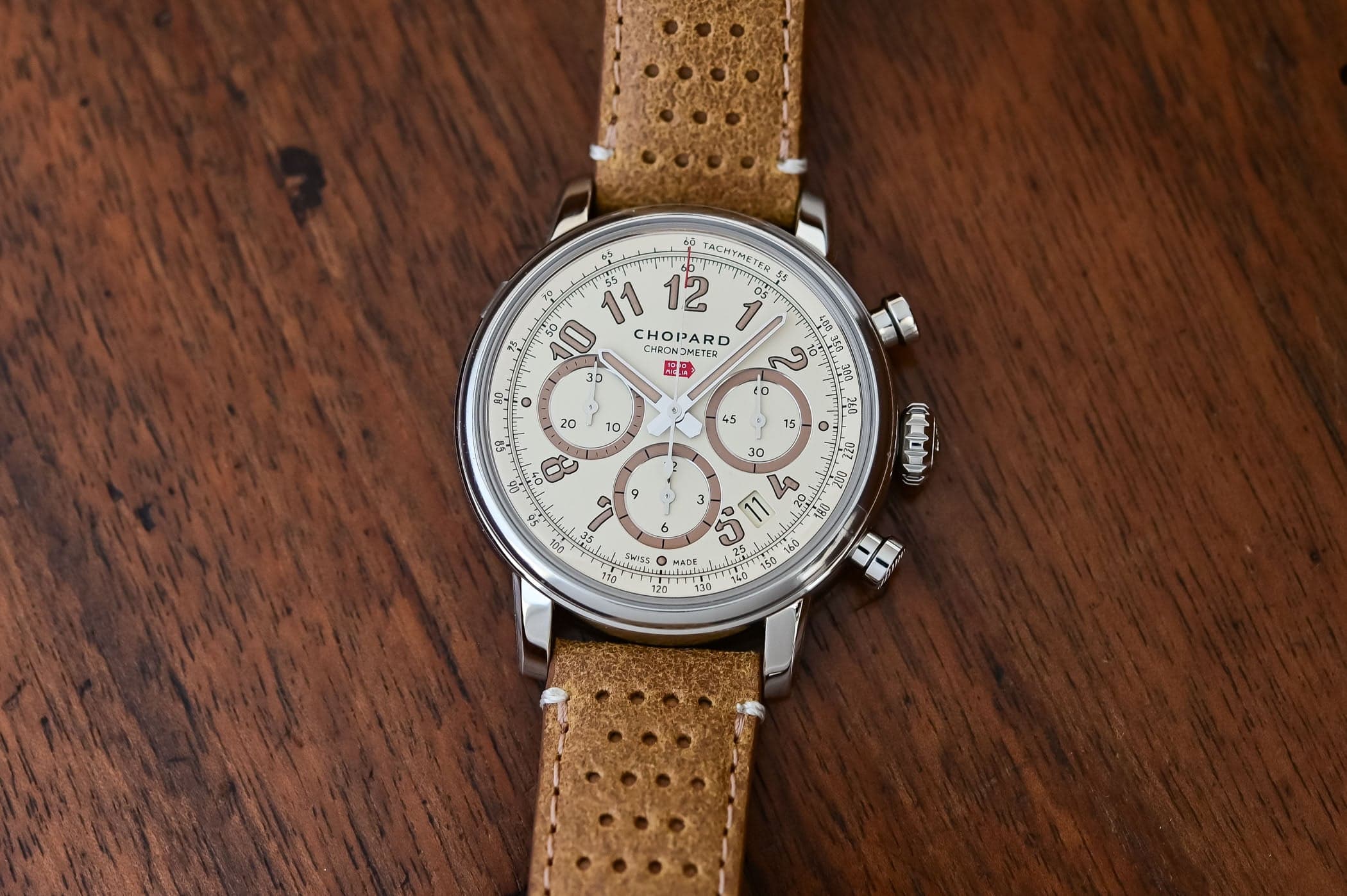 Chopard Mille Miglia Classic Chronograph Raticosa ref. 168619-3020 at an angle on dark wood, a 40.5mm Lucent Steel case with an eggshell tri-compax dial, taupe sub-dial rings, printed tachymeter scale and red 1000 Miglia arrow, on a tan perforated leather racing strap