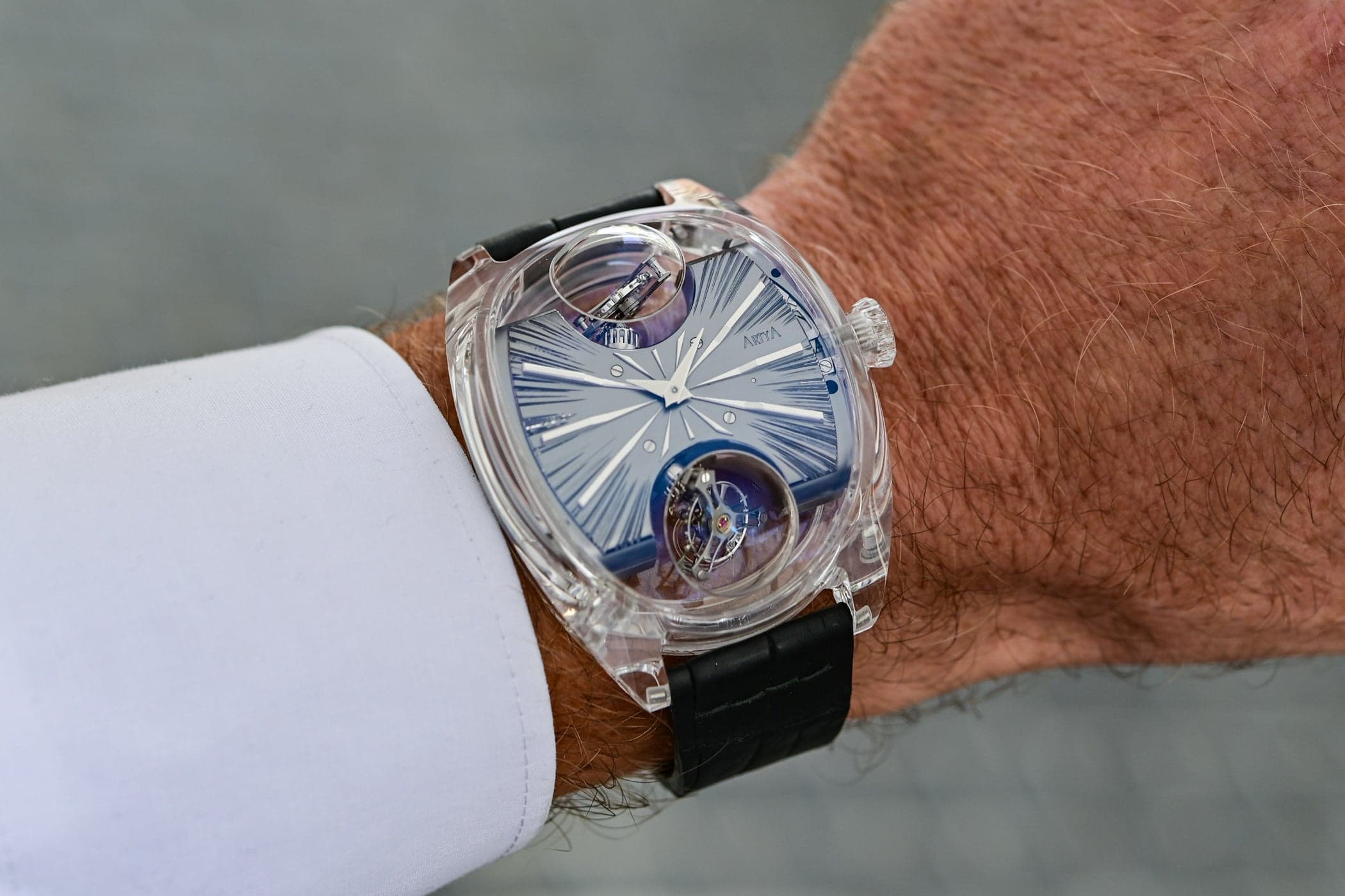 The ArtyA Complexity Metiers d'Art on the wrist, a transparent sapphire case with a blue engraved dial and two inclined tourbillons under sapphire domes at 12 and 6 o'clock, on a black strap