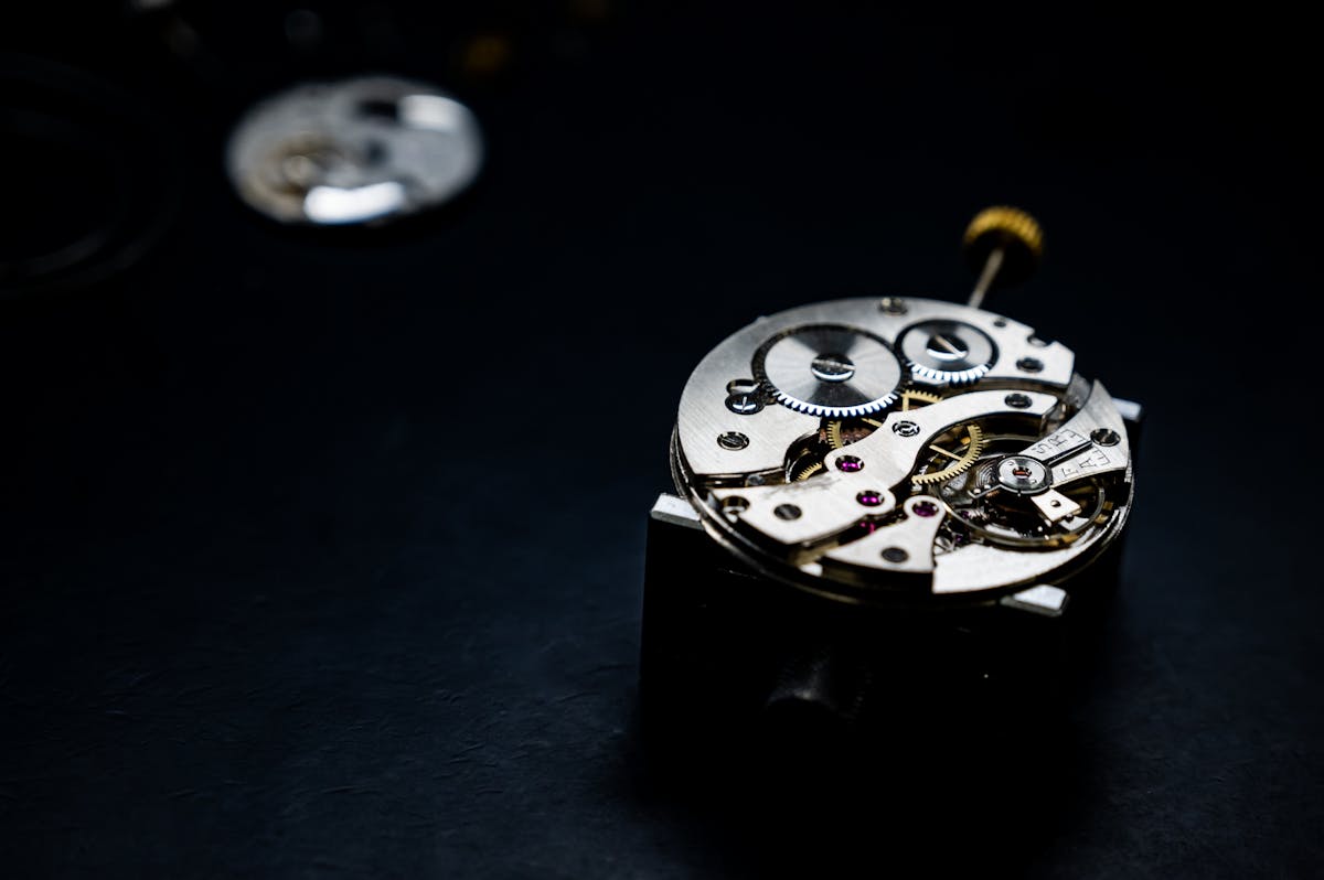 Mechanical watch movement on a dark surface with gear train and ruby jewels visible, representing the watchmaking industry context for a secondary market story on Patek Philippe, Rolex, and Audemars Piguet