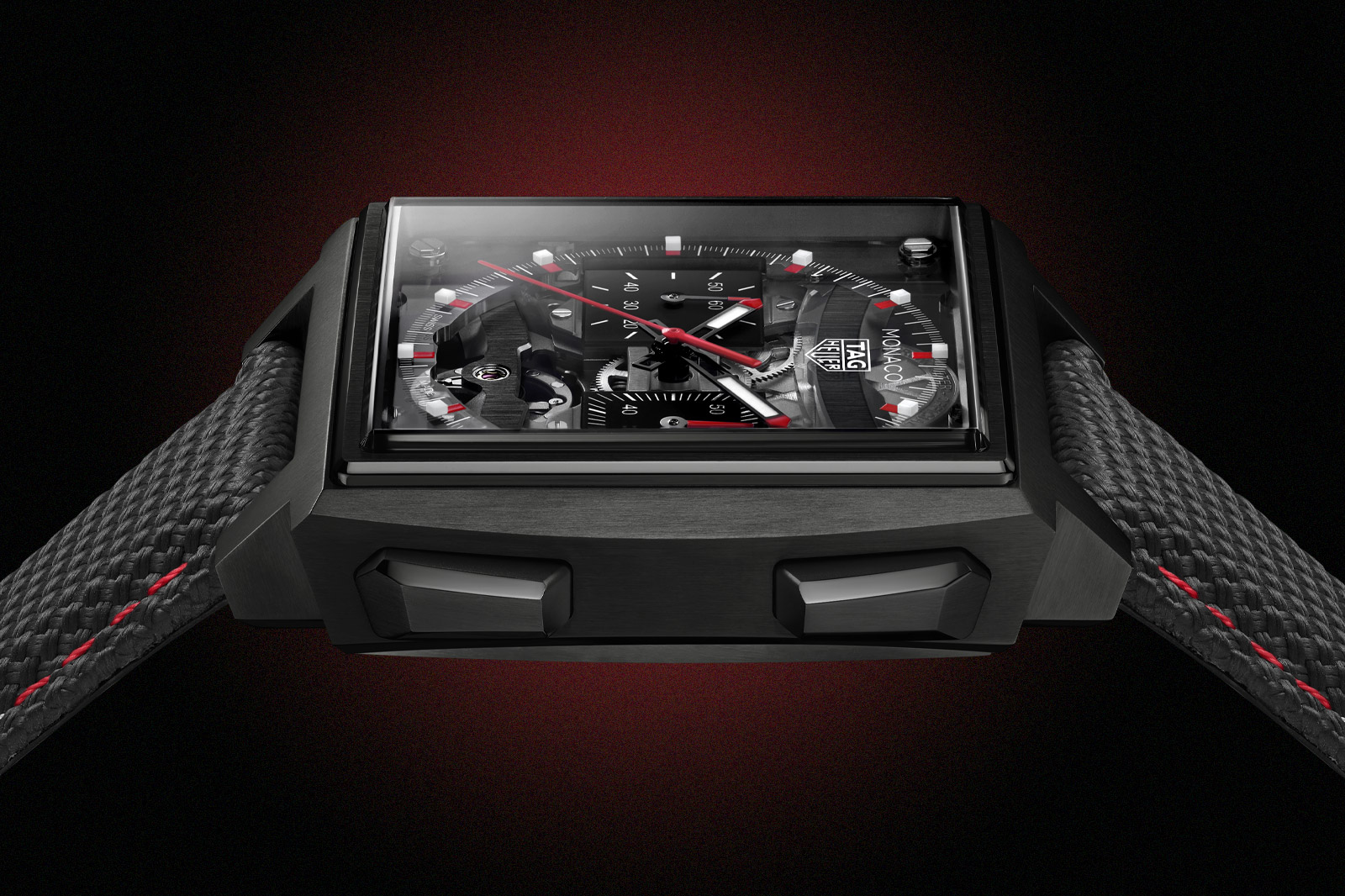 Black DLC-coated variant of the Monaco Evergraph (sibling reference CEW5180), side profile showing the titanium case with DLC treatment, black dial, red chronograph seconds hand, and grey rubber strap with red centre stitching