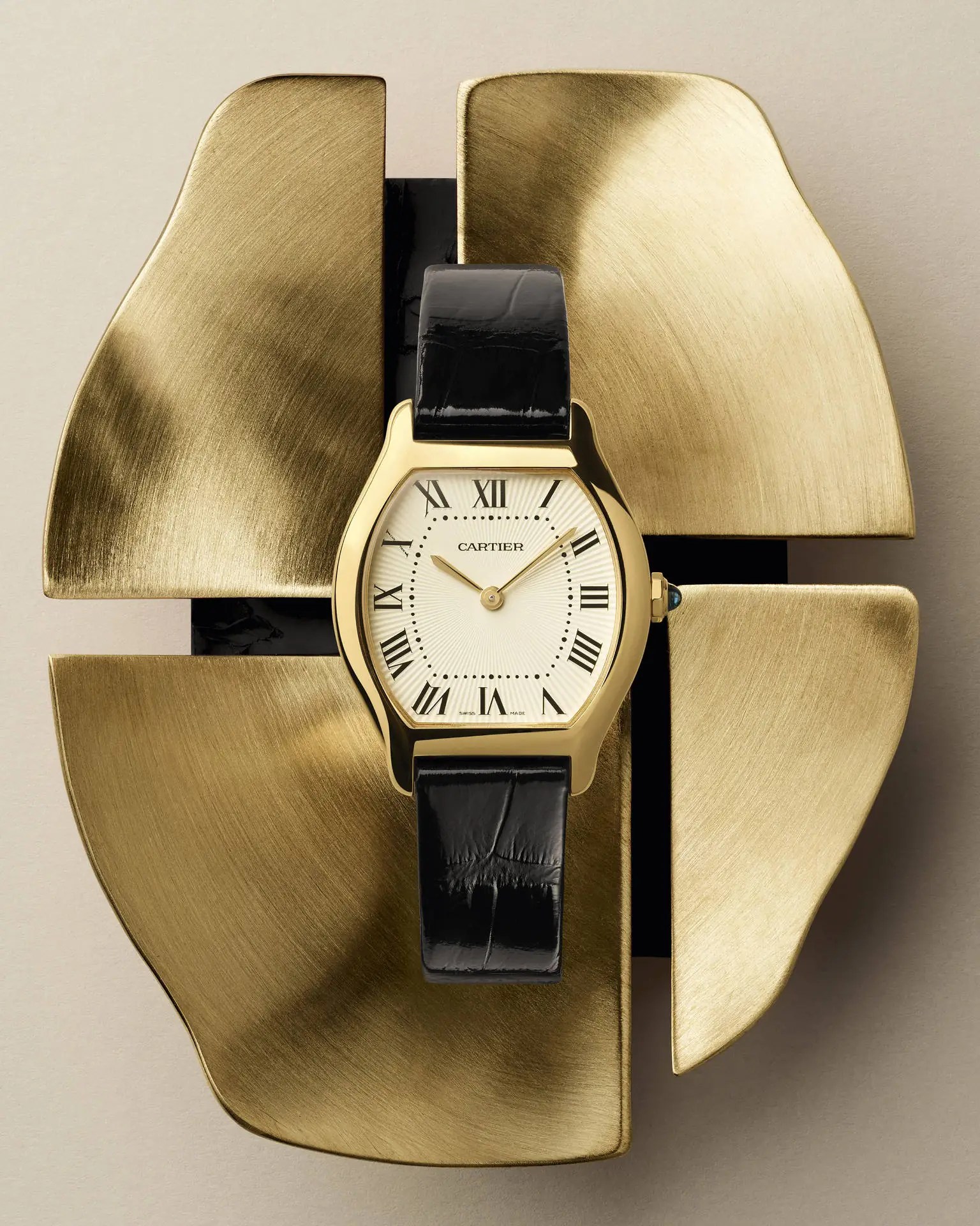 Yellow gold Tortue with ivory dial, Roman numerals and apple-shaped blued steel hands, displayed on a brushed gold sculptural backdrop