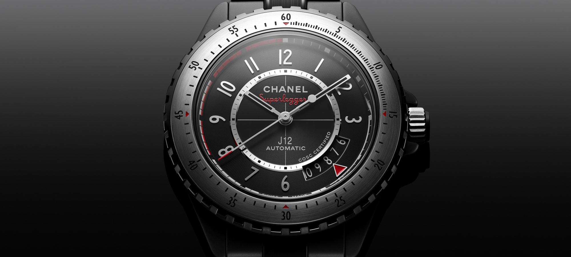 Dial macro of the Chanel J12 Superleggera 42mm, black dial with Superleggera signature in red under the CHANEL logo, red-painted index track from 7 to 10 minutes, central sweep seconds hand, cyclops-less date window at 4 o'clock with a red arrow pointing to the current date, brushed-steel bezel with red triangular markers