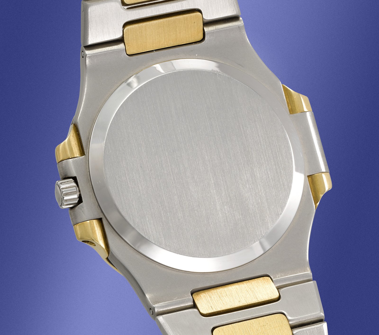 Polished smooth steel caseback of the Patek Philippe Nautilus 3700/1JA viewed against a blue background, the brushed steel inner case and yellow gold centre links of the integrated bracelet visible at the upper edge, the screw-down crown at three o'clock framed by the right-side gold spacer