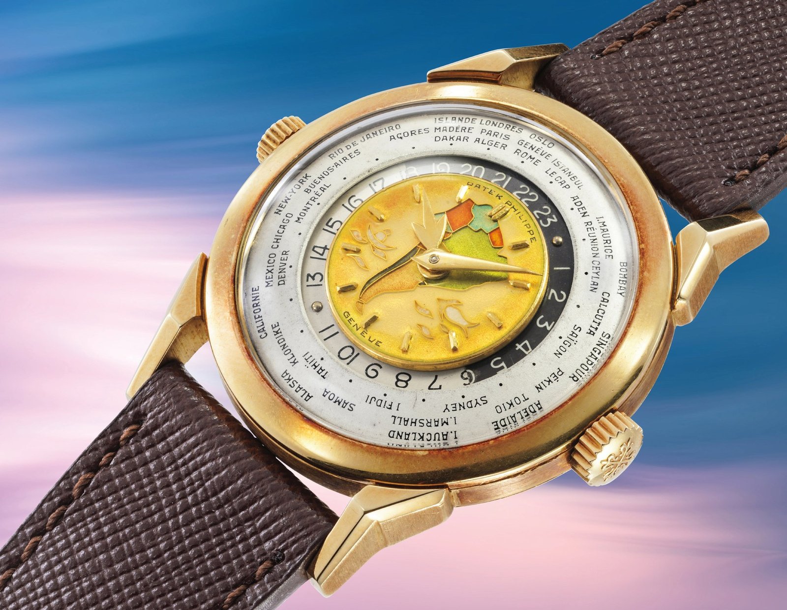 Patek Philippe 2523 'Doppia Corona Policromo' photographed at an angle showing the polychrome cloisonné enamel dial, the second crown at four o'clock used to advance the world-time city ring, applied yellow gold hour markers and brown leather strap