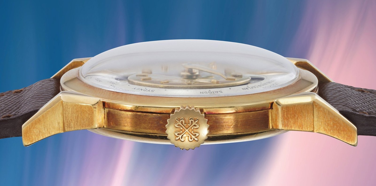 Patek Philippe 2523 case profile showing the domed plexiglass crystal, polished yellow gold case flank, signed Patek crown at three o'clock and second world-time crown adjuster, brown leather strap edges visible