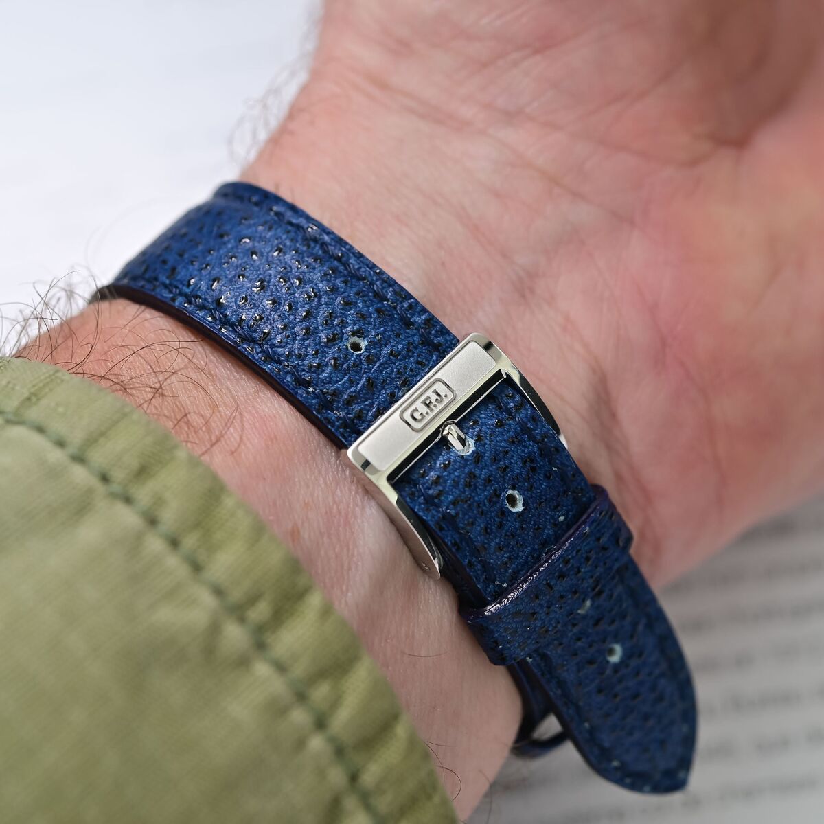 Wrist shot showing the platinum pin buckle engraved with the G.F.J. initials on the indigo Kaihara denim strap
