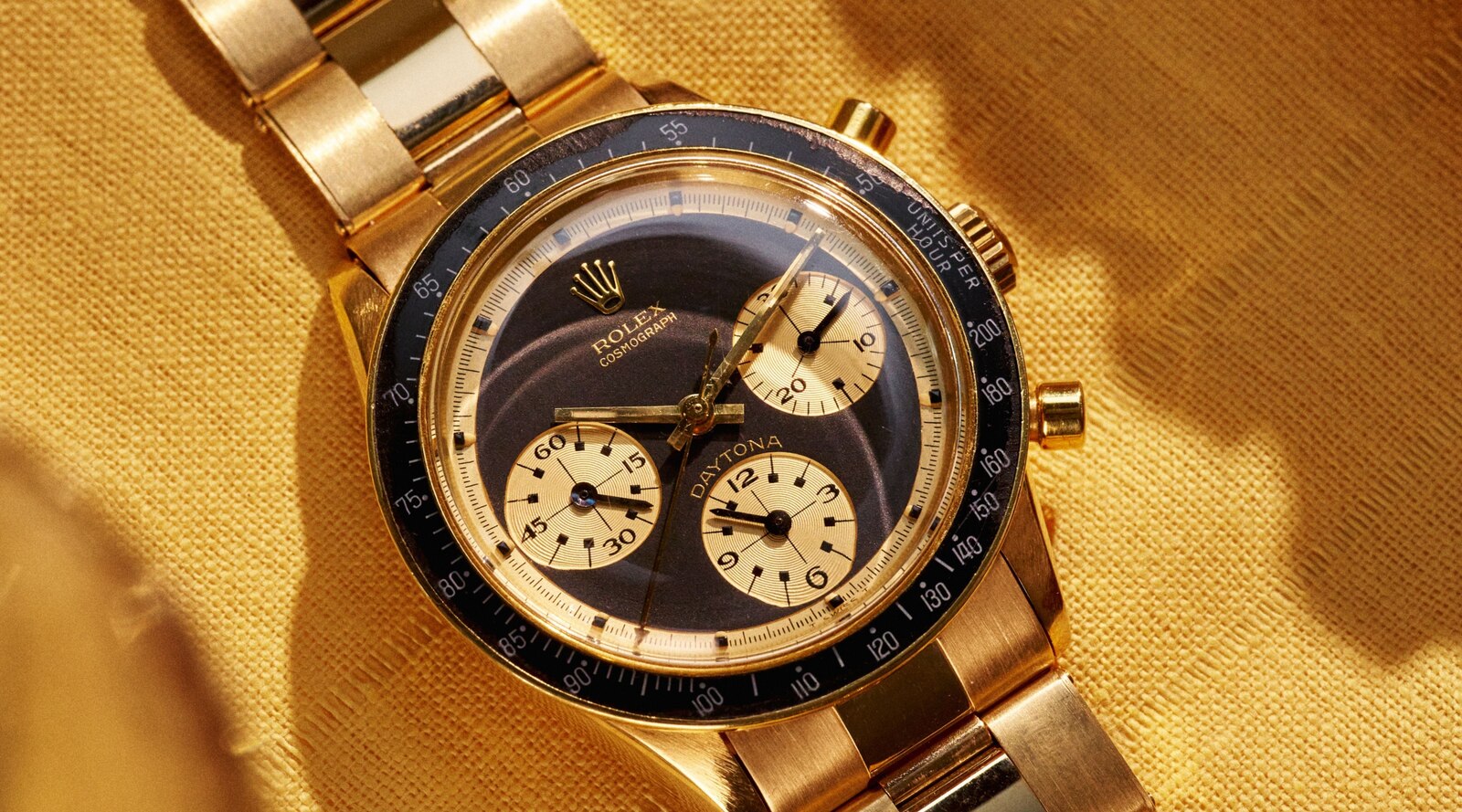 Rolex Cosmograph Daytona reference 6241 'John Player Special' in yellow gold, black dial with gold registers and black acrylic tachymeter bezel, photographed on a gold bracelet against a yellow fabric ground