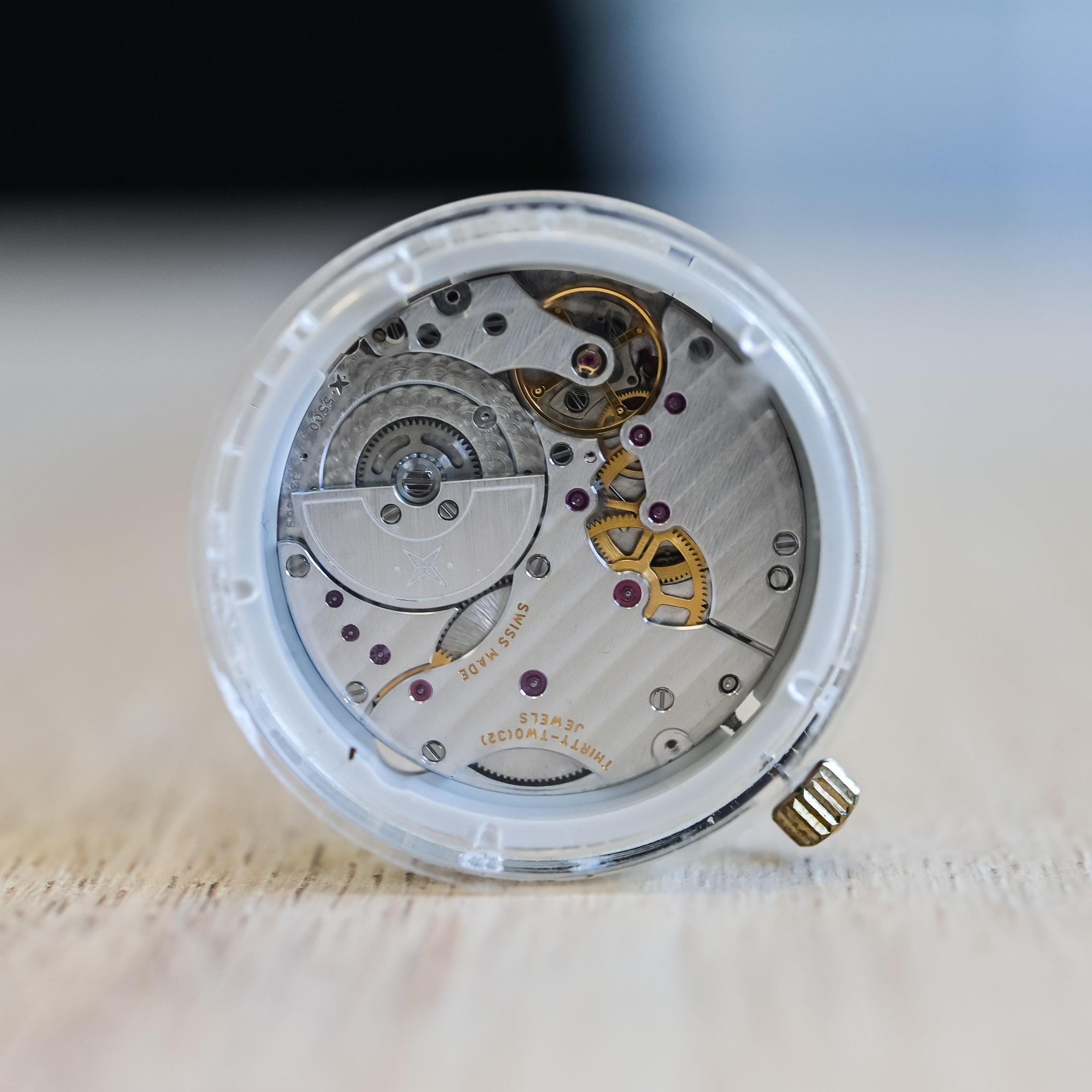 VMF 5500 seen at an angle in its transparent casing ring against a dark background, 5500 engraving visible on the mainplate edge, gold gear train and crown on the right