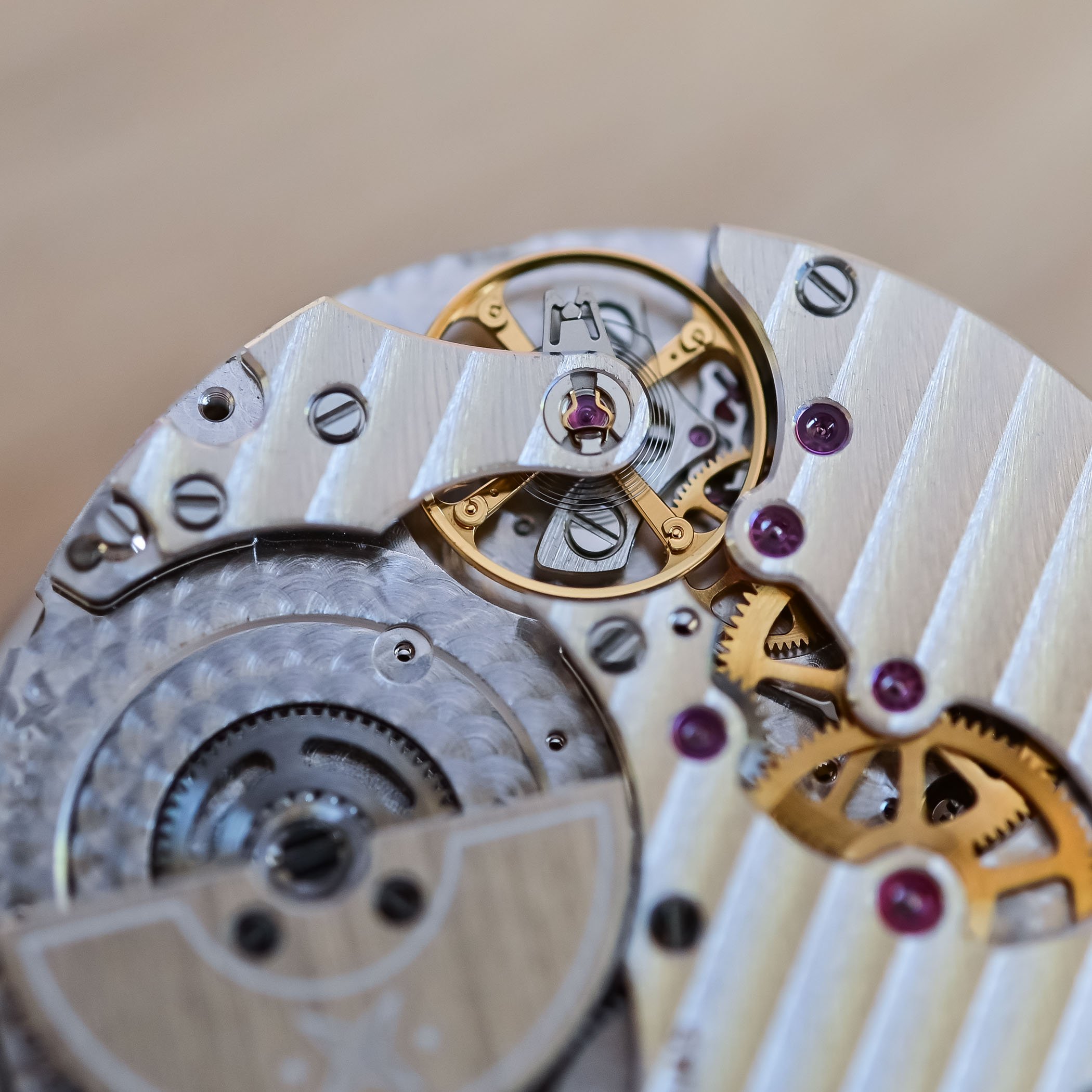 Macro of the VMF 5500 balance bridge and gold wheels, with the guilloché edge of the micro-rotor at lower left and ruby jewels in polished sinks