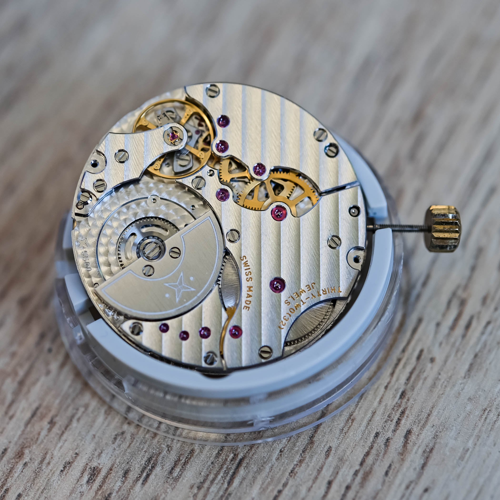 VMF 5500 movement three-quarter view on a wooden surface, Côtes de Genève striping across the bridges, star-logo micro-rotor at left and winding stem with crown at right