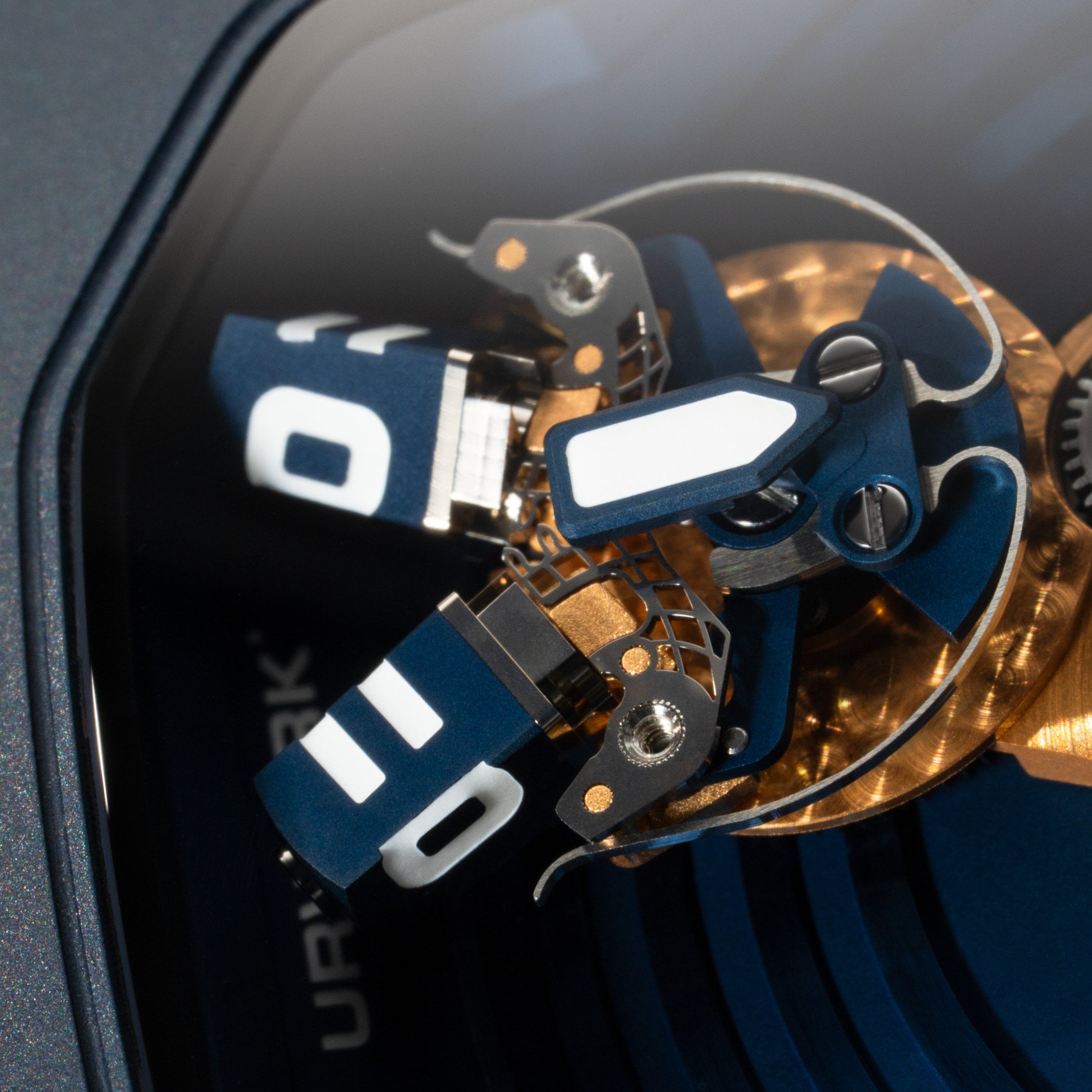 Macro of the splitting hour cubes and the gold-plated carousel gearing beneath the shaped sapphire crystal, with the URWERK engraving along the case edge