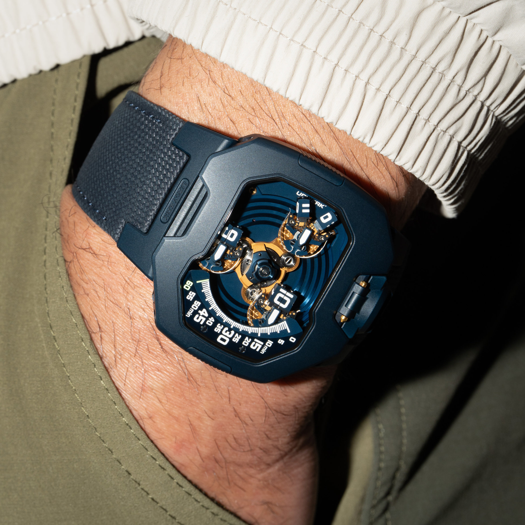 Angled wrist shot of the UR-120 Blue Planet showing the blue PVD case flank, the gold satellite display and the blue ballistic-textured calfskin strap