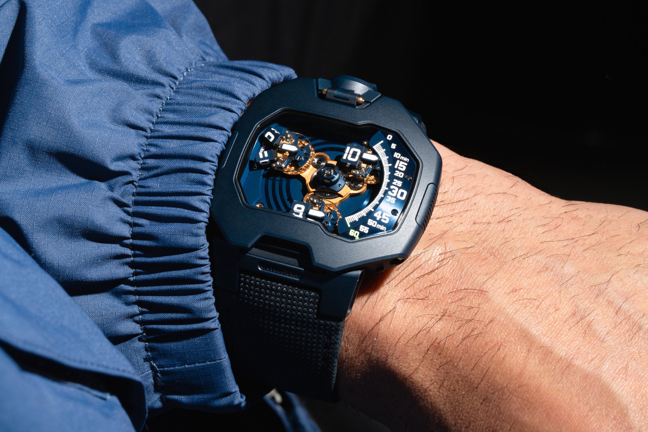 Urwerk UR-120 Blue Planet on the wrist, 47mm by 44mm sandblasted steel case with a blue PVD coating, the satellite hour display with gold-plated carousel and splitting cubes visible through the shaped sapphire crystal, blue ballistic-textured calfskin strap