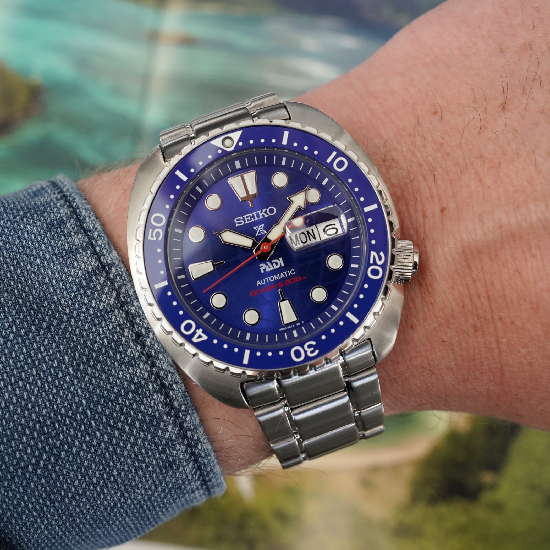 The HBB002 worn on the wrist with a blue cuff, showing the cushion steel case, blue dial and bezel and the steel bracelet