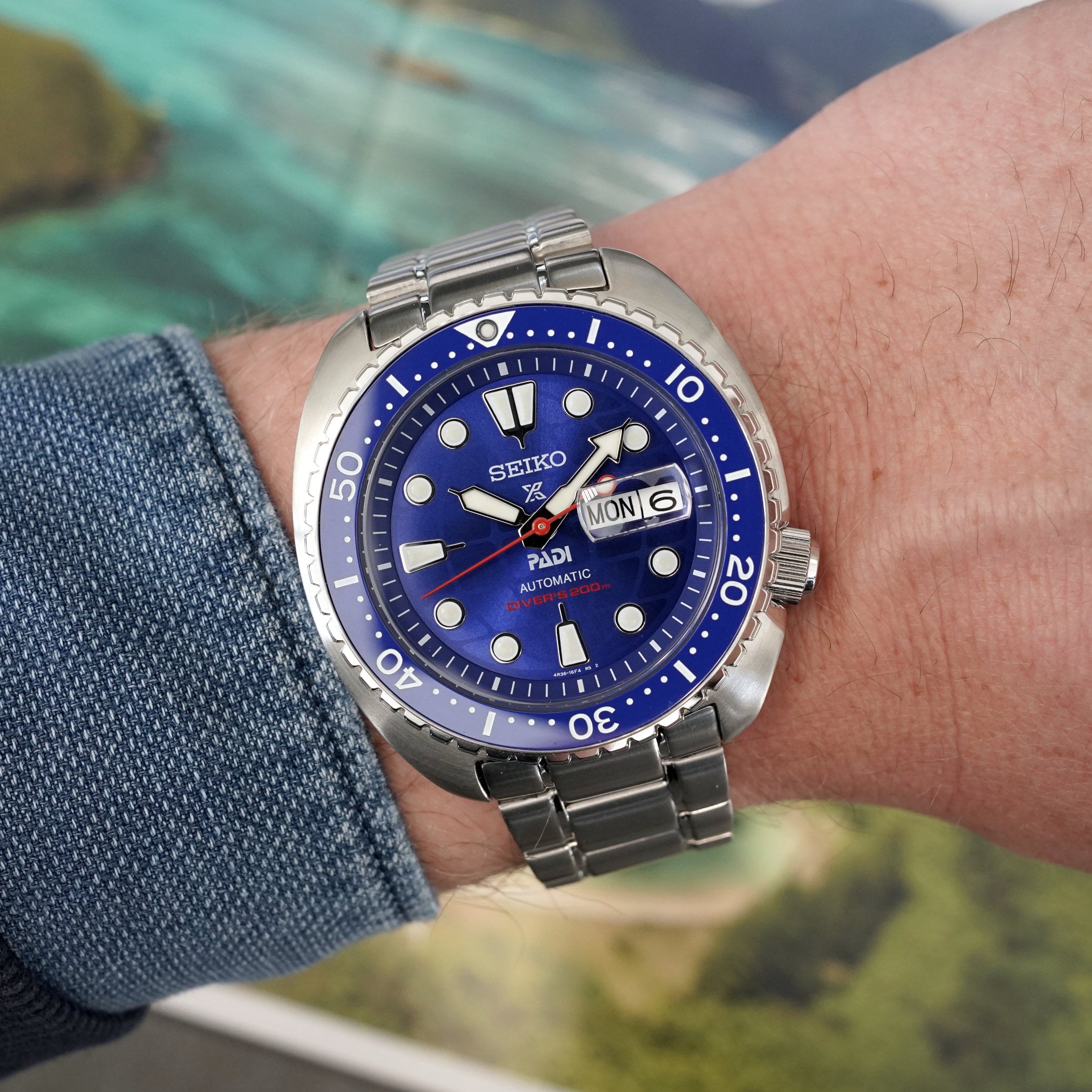 Wrist shot of the HBB002 from a lower angle, blue sunburst dial and bezel catching the light, day-date at three on the steel bracelet