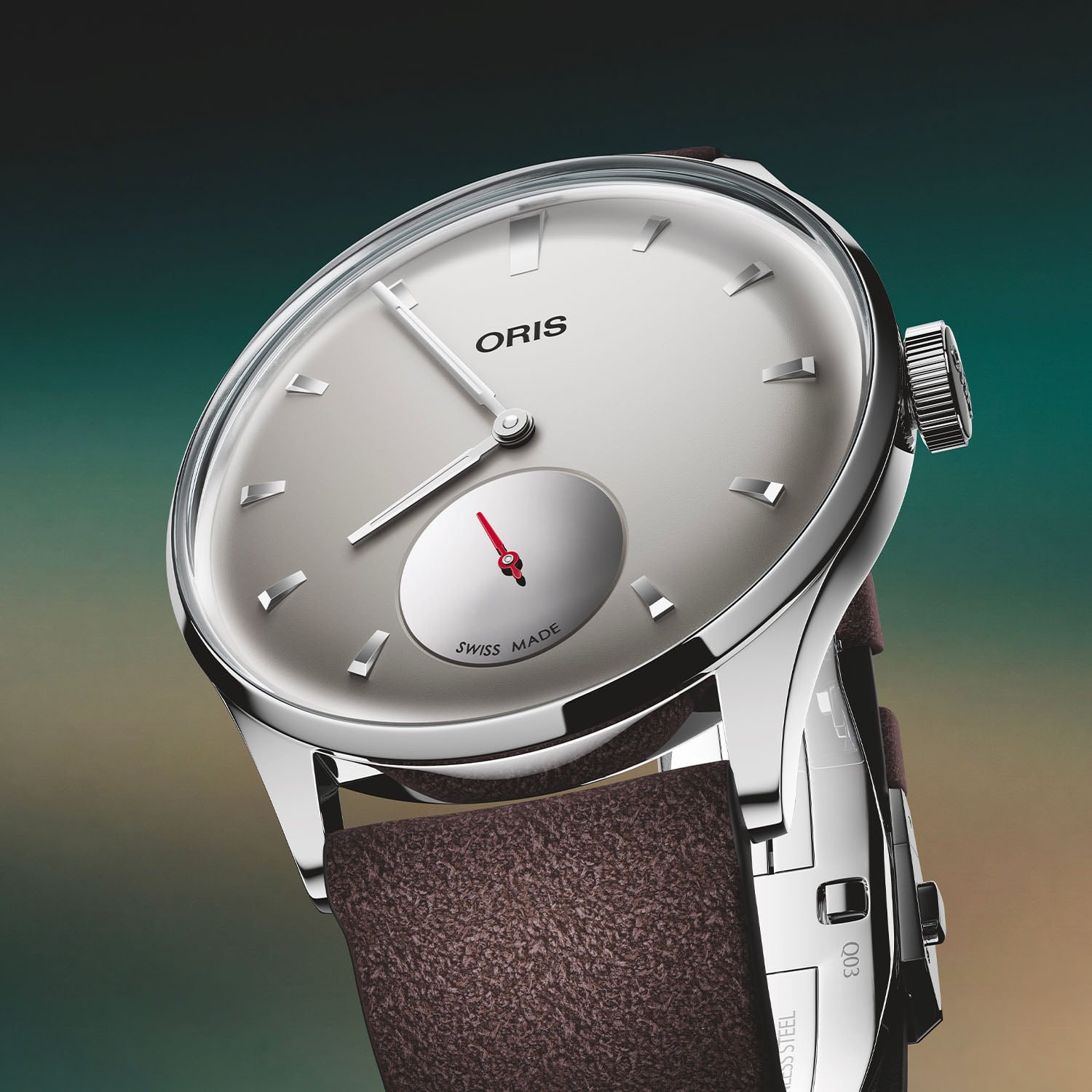 Oris Hölstein Edition 2026 at a three-quarter angle, polished 39.5mm stainless steel case, light grey dial with applied polished wedge markers and a mirror-finish small-seconds sub-dial with a red hand at six, on a brown suede strap