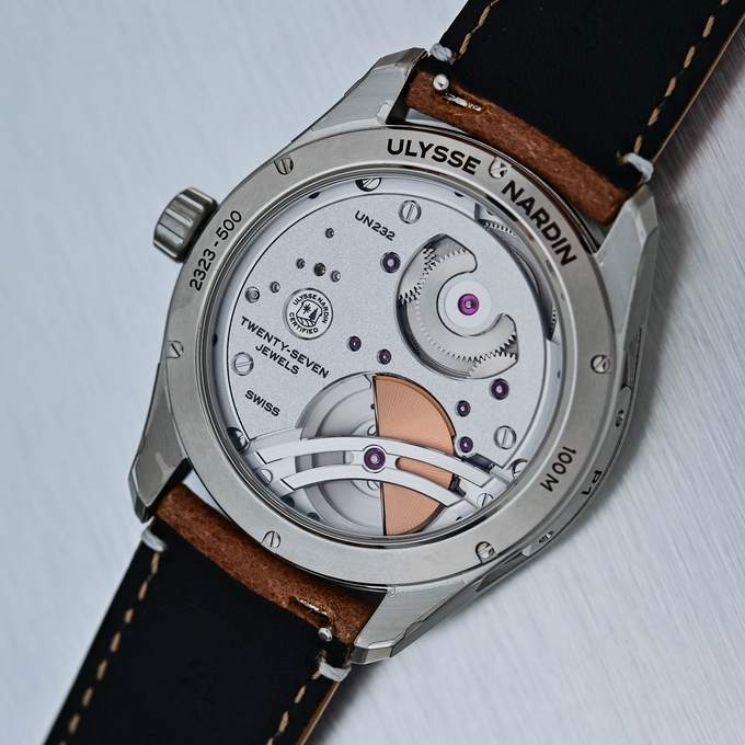Sapphire caseback of the Ulysse Nardin Freak X 2026, reference 2323-500, showing the UN-232 movement with its rose gold micro-rotor, the engraving TWENTY-SEVEN JEWELS and 100M, on a brown calfskin strap