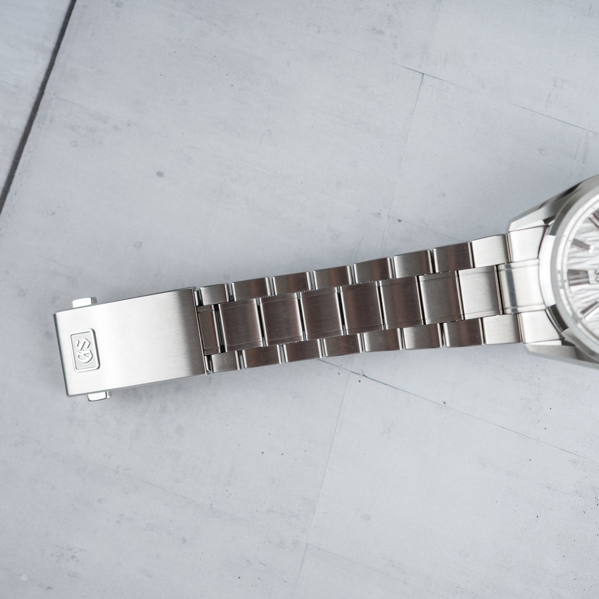 The new more-tapered bracelet and folding clasp of the Grand Seiko Evolution 9 Hi-Beat seen from above, the clasp cover stamped with the Grand Seiko emblem