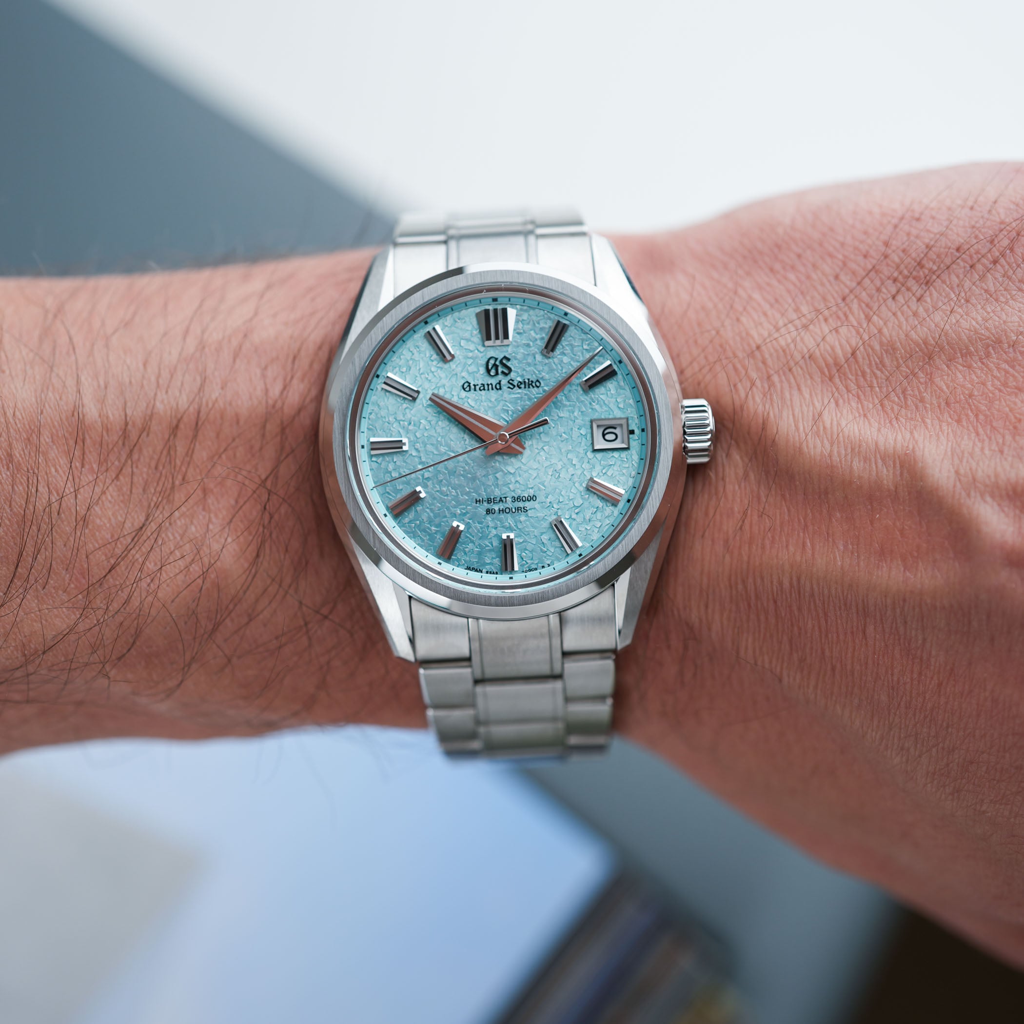 The Grand Seiko Evolution 9 Hi-Beat Genbi Valley SLGH035 on the wrist, its pale aqua dial carrying a water-like texture, applied faceted markers, a date at three o'clock and the line HI-BEAT 36000 80 HOURS