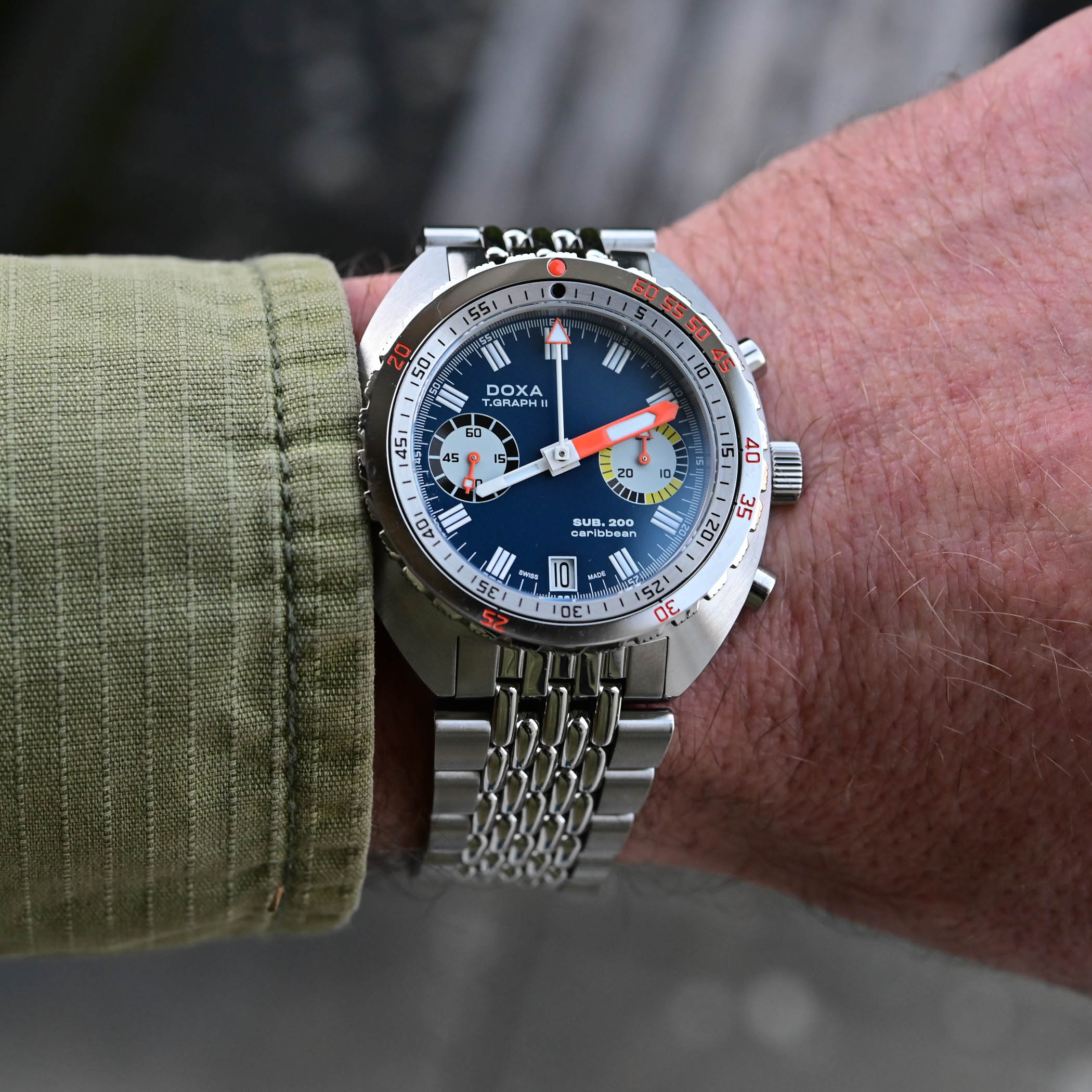 Doxa SUB 200 T.Graph II Caribbean with a dark blue dial and orange chronograph hand on a steel beads-of-rice bracelet, worn on the wrist, the black-and-orange bezel and SUB. 200 caribbean text visible