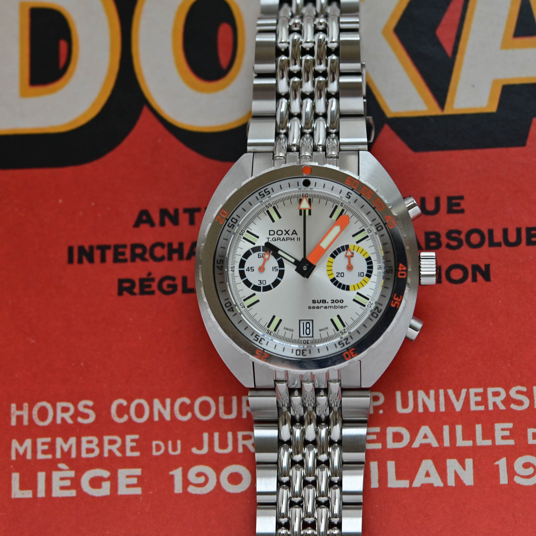 Doxa SUB 200 T.Graph II Searambler with a sunburst silver dial on a steel beads-of-rice bracelet, two subdials and date at 6, photographed on a vintage Doxa brochure