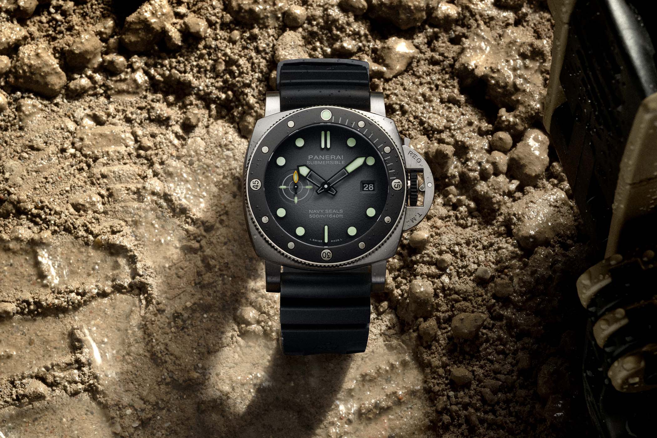 Panerai Submersible Navy SEALs PAM01738 with a brushed steel case, black ceramic dive bezel with a luminous dot at noon, grey gradient dial reading SUBMERSIBLE NAVY SEALS 500m/1640ft, date at 3 and a black rubber strap, lying on wet sand