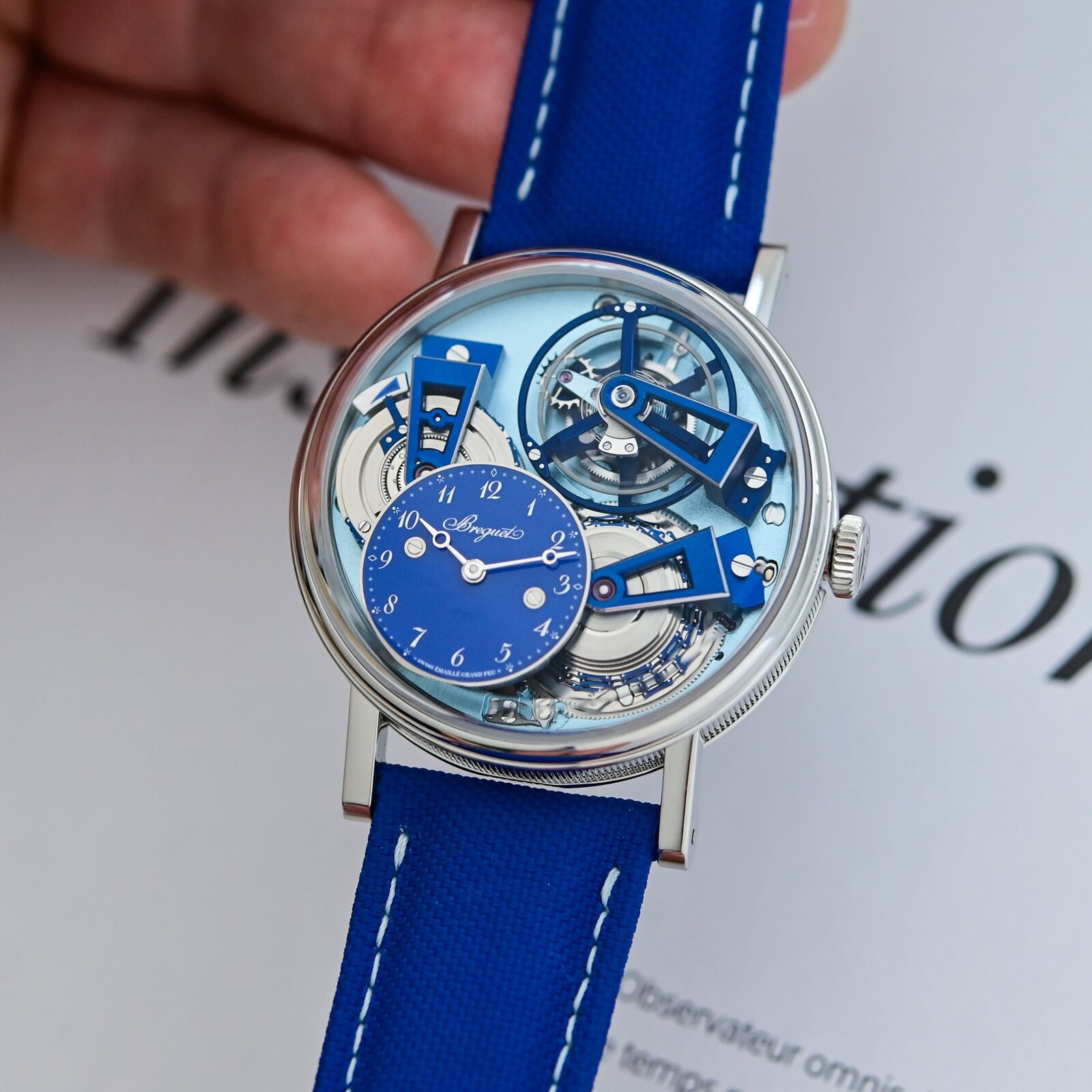 The Breguet Tradition Tourbillon 7047PT held in hand, its exposed chain-and-fusee transmission, tourbillon and bridges finished in Bleu de France blue with an off-centre blue enamel time sub-dial, on a blue strap