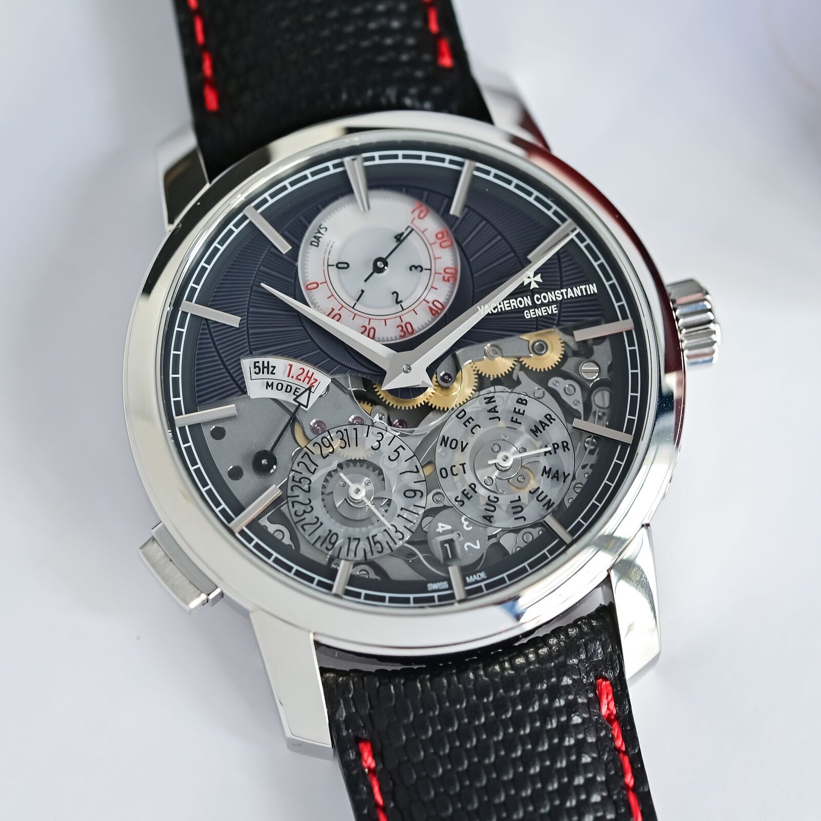 Three-quarter view of the platinum Vacheron Constantin Twin Beat Perpetual Calendar on a black calfskin strap with red contrast stitching, the open dial showing the perpetual calendar sub-dials and the frequency selector at nine o'clock