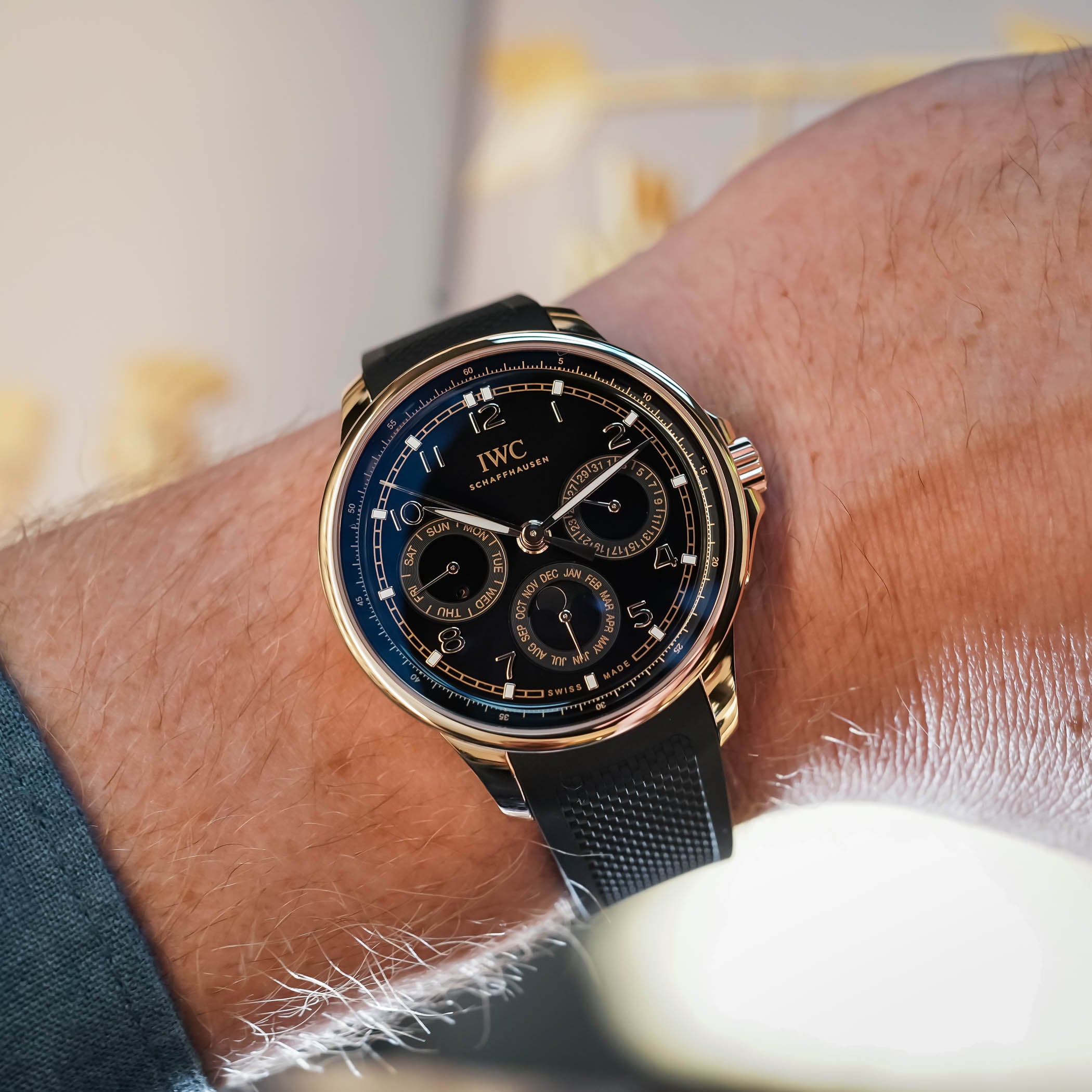 IWC Portugieser Yacht Club Perpetual Calendar 42 on the wrist with a blue shirt cuff, the Armor Gold case and black rubber strap framing the black dial's calendar sub-dials