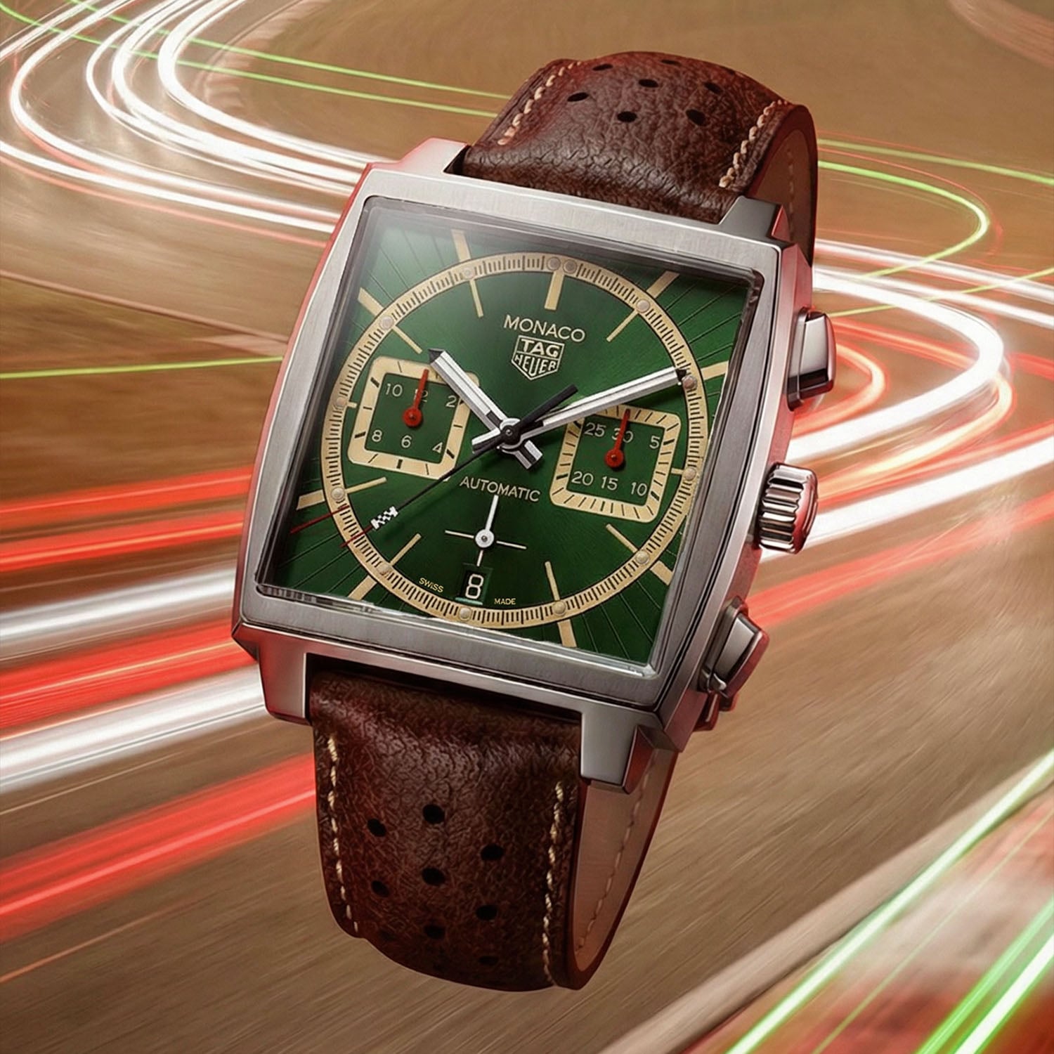 TAG Heuer Monaco x Goodwood Festival of Speed 2026 at a three-quarter angle on a motion-blurred racing background, British Racing Green dial with beige square counters, red subdial hands, steel case and brown perforated strap