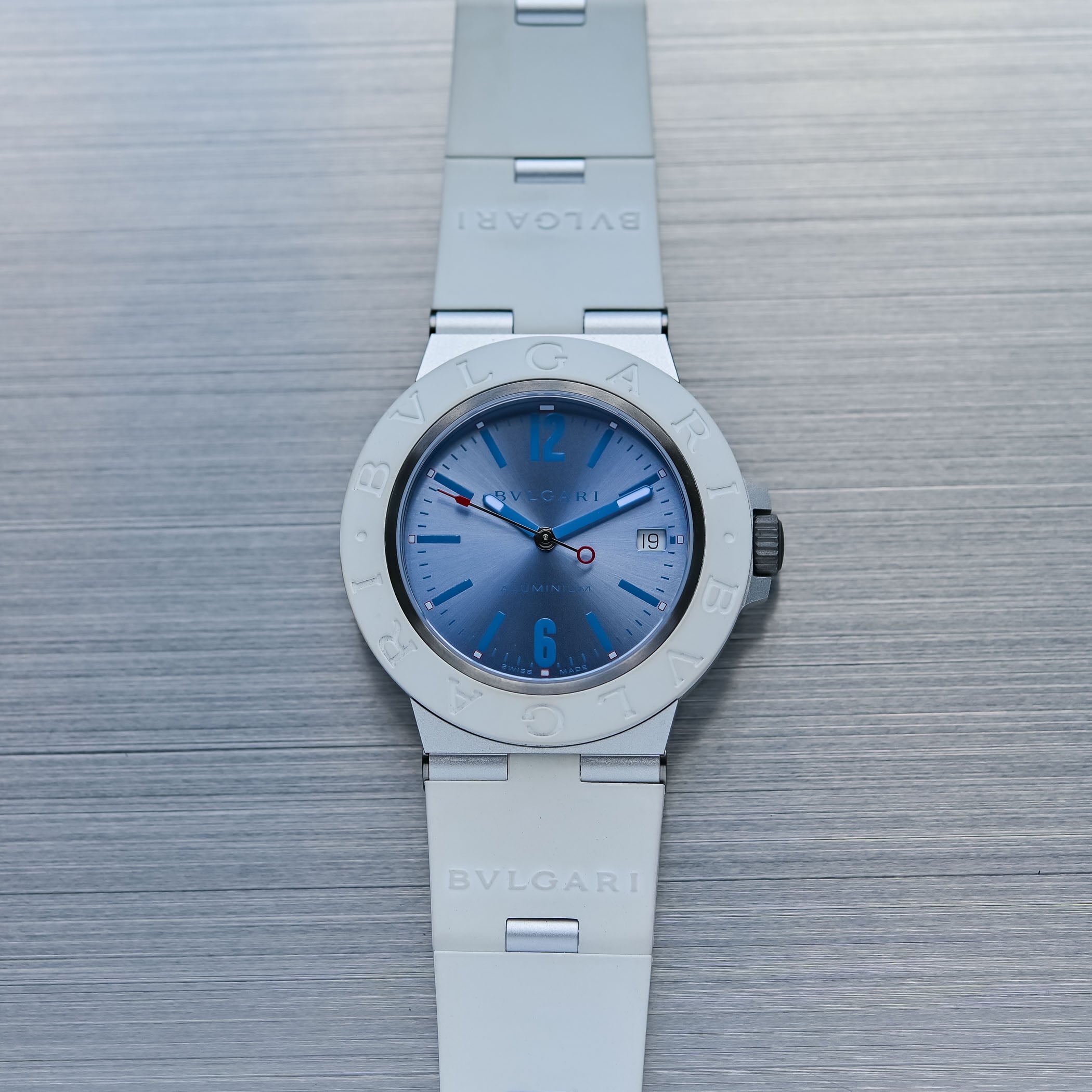 Bulgari Aluminium Ice Blue ref. 104309 flat on brushed steel, sun-brushed light blue dial with blue varnished numerals and indices, red-tipped central seconds hand with red ring counterweight, date at 3, white rubber bezel and strap with aluminium links