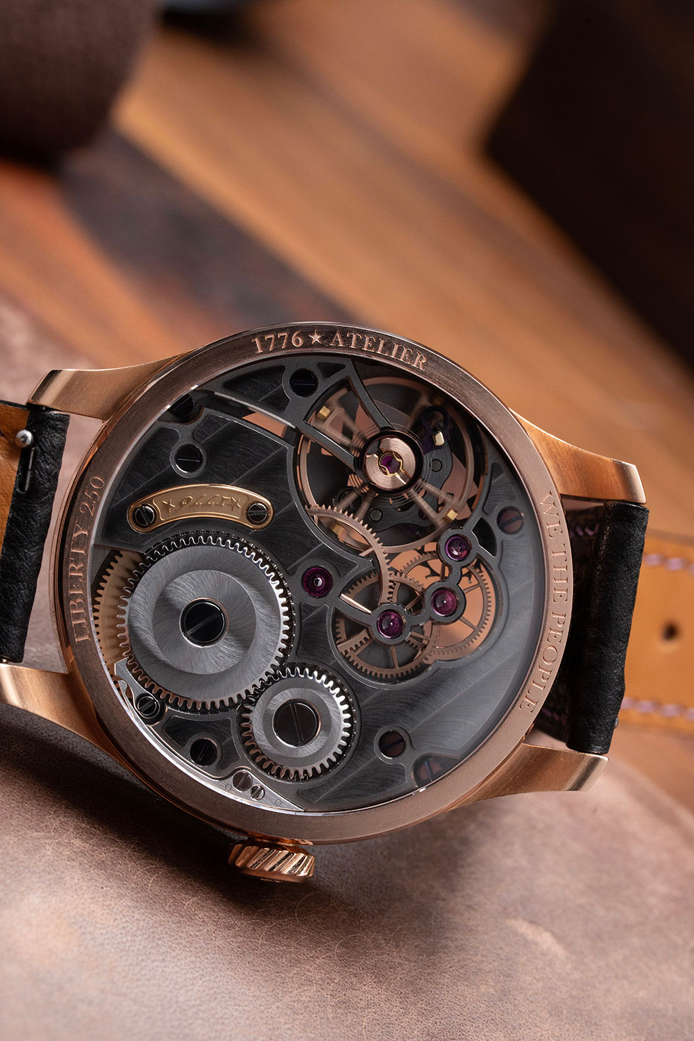 Display back of the 1776 Atelier Liberty 250, rose gold case ring engraved 1776 ATELIER, LIBERTY 250 and WE THE PEOPLE, showing the openworked grey bridges, twin ratchet and crown wheels, gold serial plaque and bevelled gear train