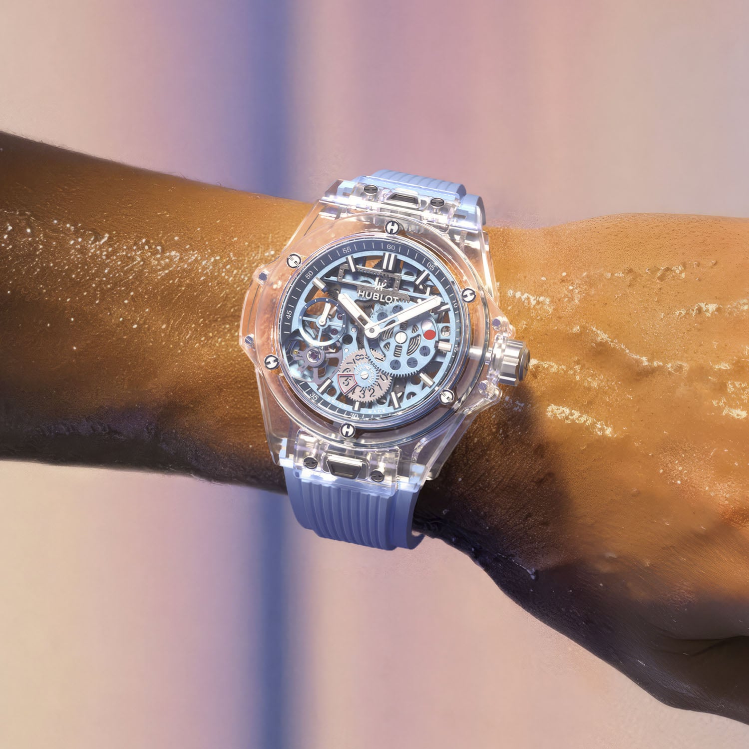 The Big Bang Sapphire Sky Blue worn on a wet forearm, transparent sapphire case and sky-blue skeleton dial with the red low-reserve marker visible, on the sky-blue rubber strap