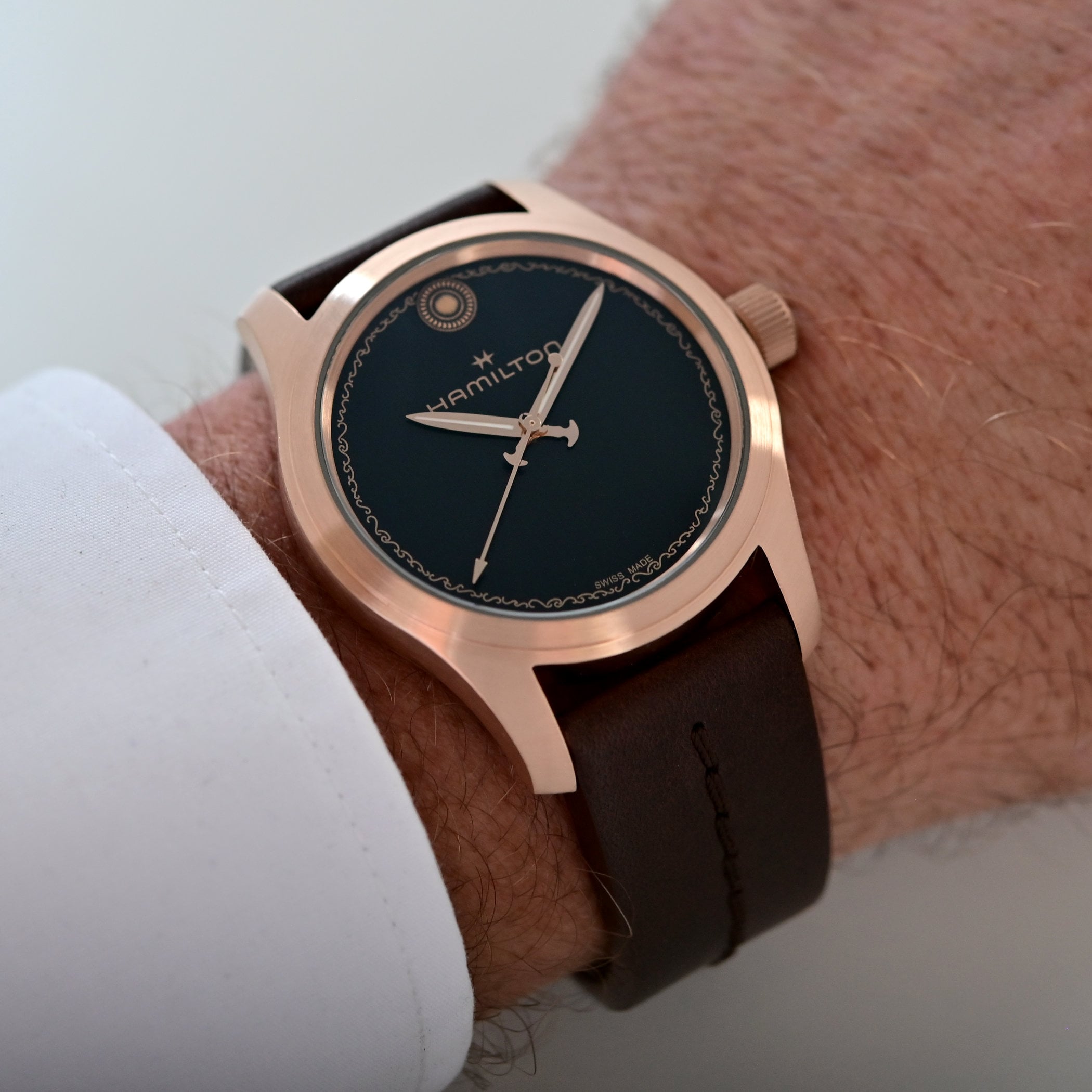 The Hamilton Khaki Field Odyssey worn on a wrist below a white shirt cuff, showing the bronze case profile, the black dial with its wave frieze and rivet marker at 12, and the brown leather strap