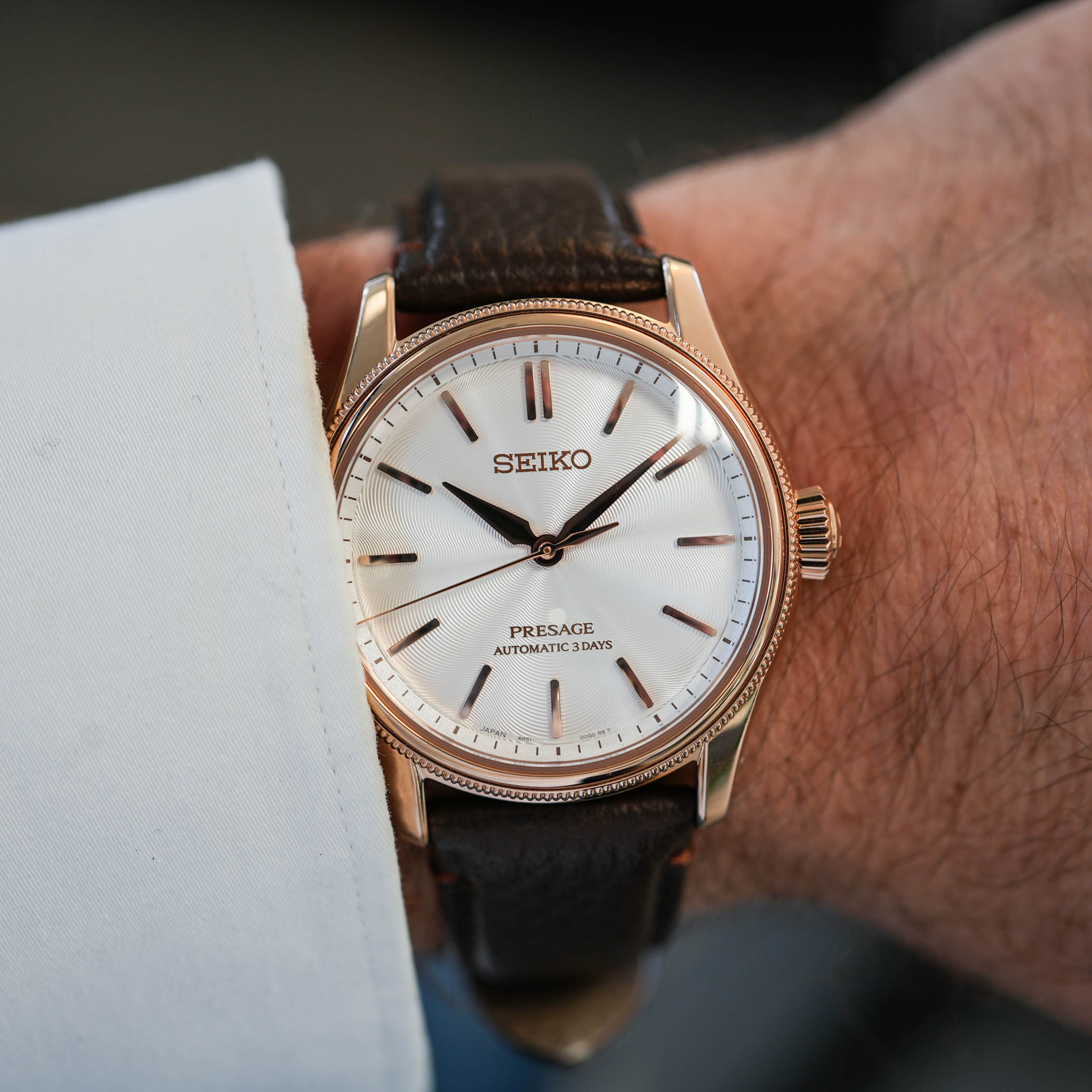 The limited edition HCC008 on the wrist below a white shirt cuff, pink-gold-plated case with beaded bezel, pearl-coated white silk-textured dial with rose-gold baton markers and hands, on a dark brown grained leather strap
