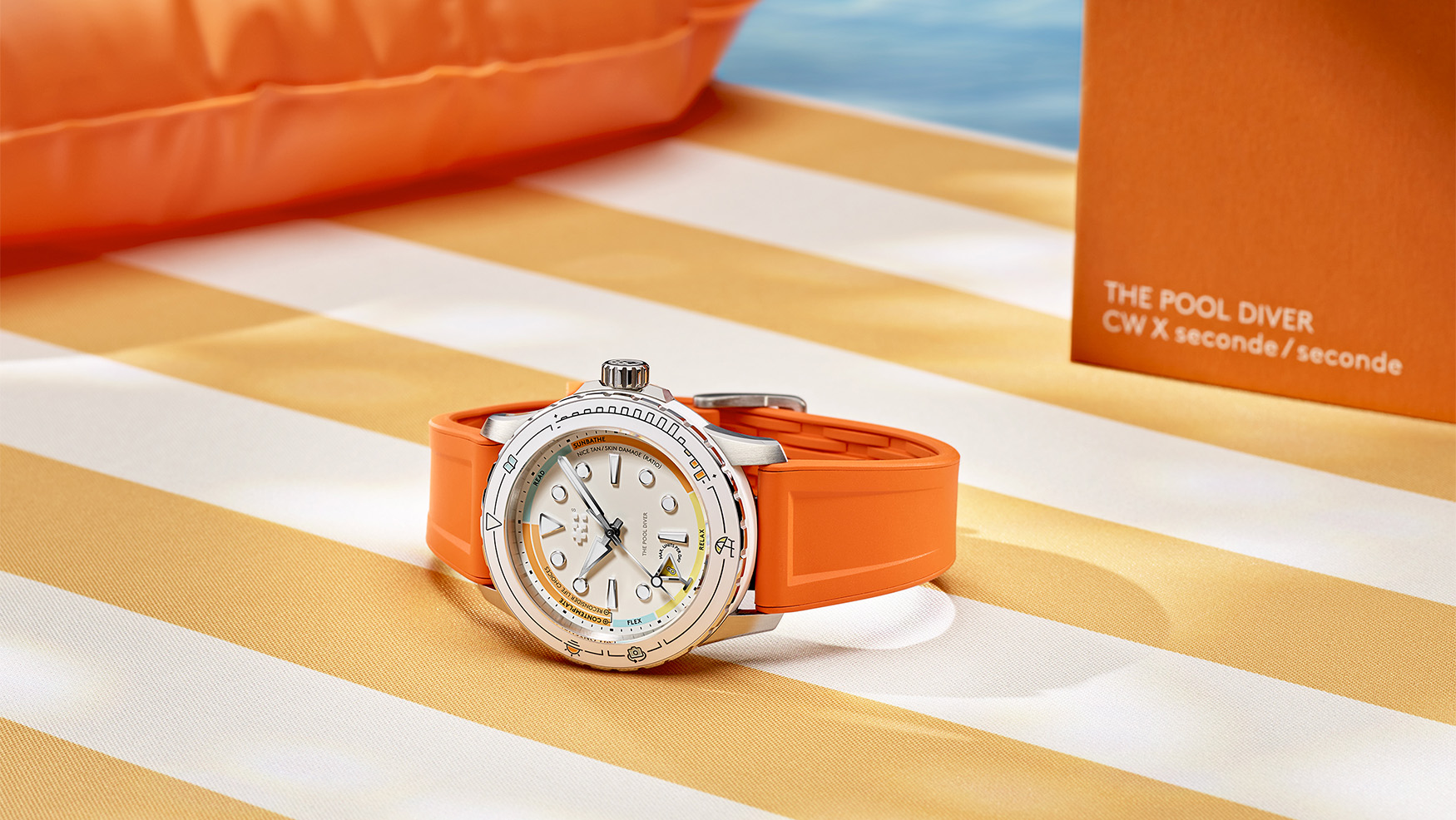 Christopher Ward C60 Pool Diver on an orange rubber strap beside an inflatable pool ring and a box reading THE POOL DIVER, CW x seconde/seconde, its white dial and bezel printed with holiday activity labels