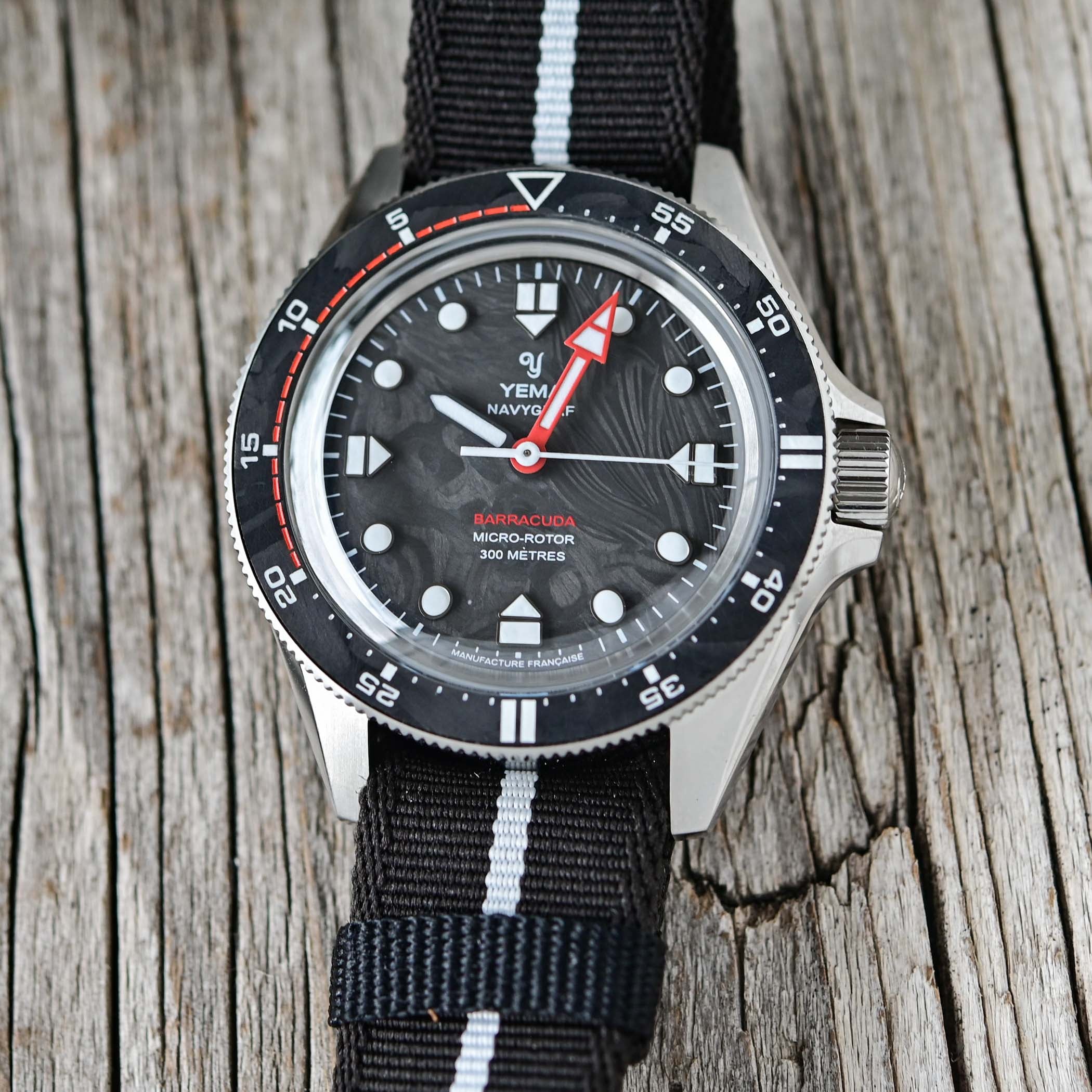 Straight-on view of the Yema Navygraf Barracuda CMM.20 dial, marbled forged carbon surface, applied lume markers, a red arrow minute hand and red BARRACUDA text at six, inside a bezel whose first 20 minutes are marked in red