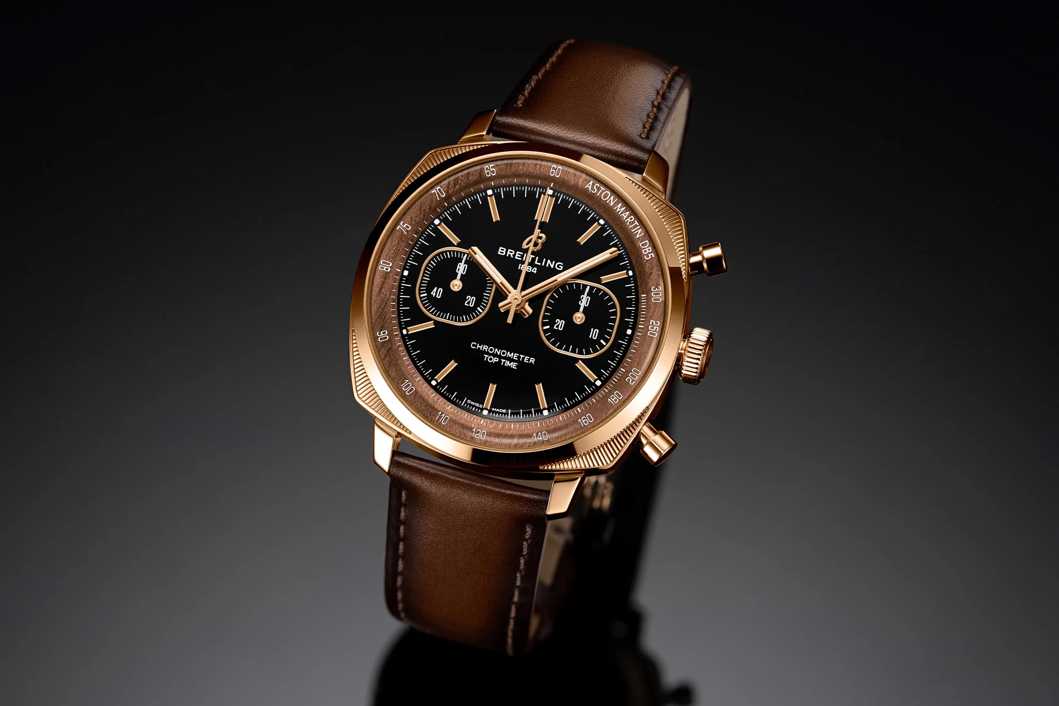 Breitling Top Time B01 Tribute to Aston Martin DB5 in 18k red gold with a black onyx dial, wood-toned tachymeter flange, gold hands and applied indices, shown at a three-quarter angle, reference RB0178131B1X1 from the 250-piece edition