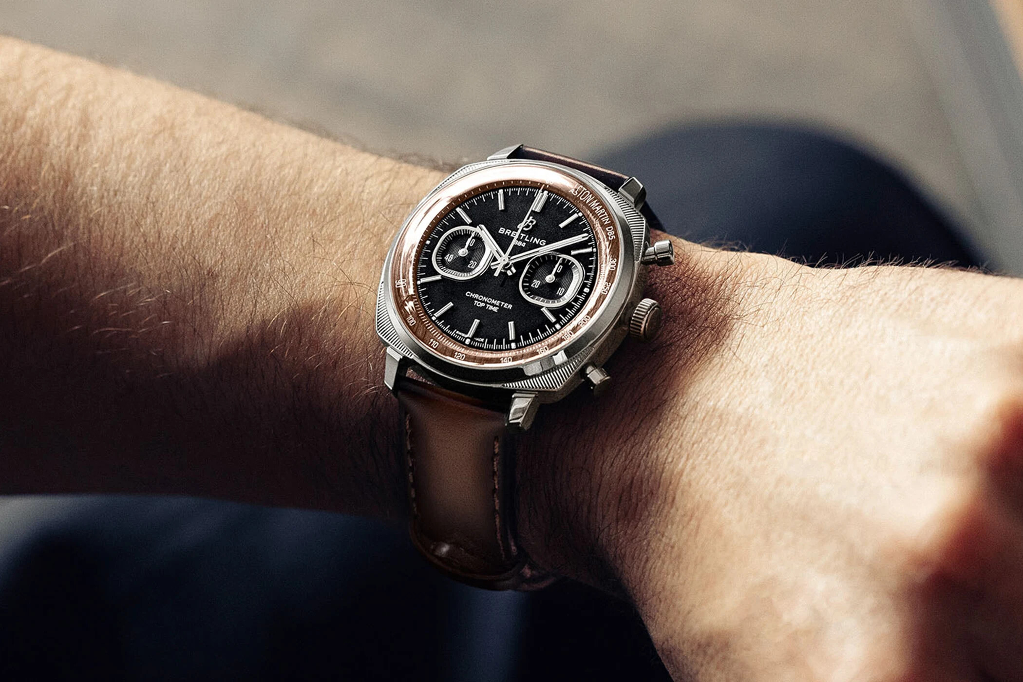 The Top Time DB5 on the wrist, steel case with a black dial, wood-toned tachymeter ring and ASTON MARTIN DB5 printed on the flange, on a brown leather strap