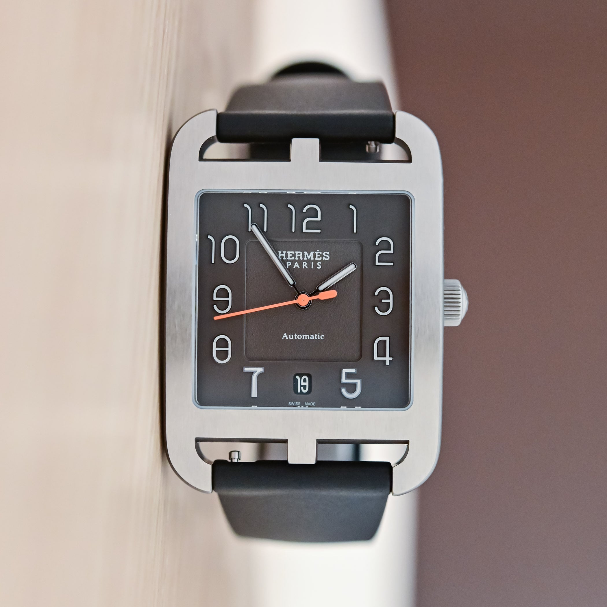 Dial of the Hermes Cape Cod Titanium, black sandblasted centre and satin outer ring, applied rhodium Arabic numerals, an orange central seconds hand and a date at 6, on a black rubber strap