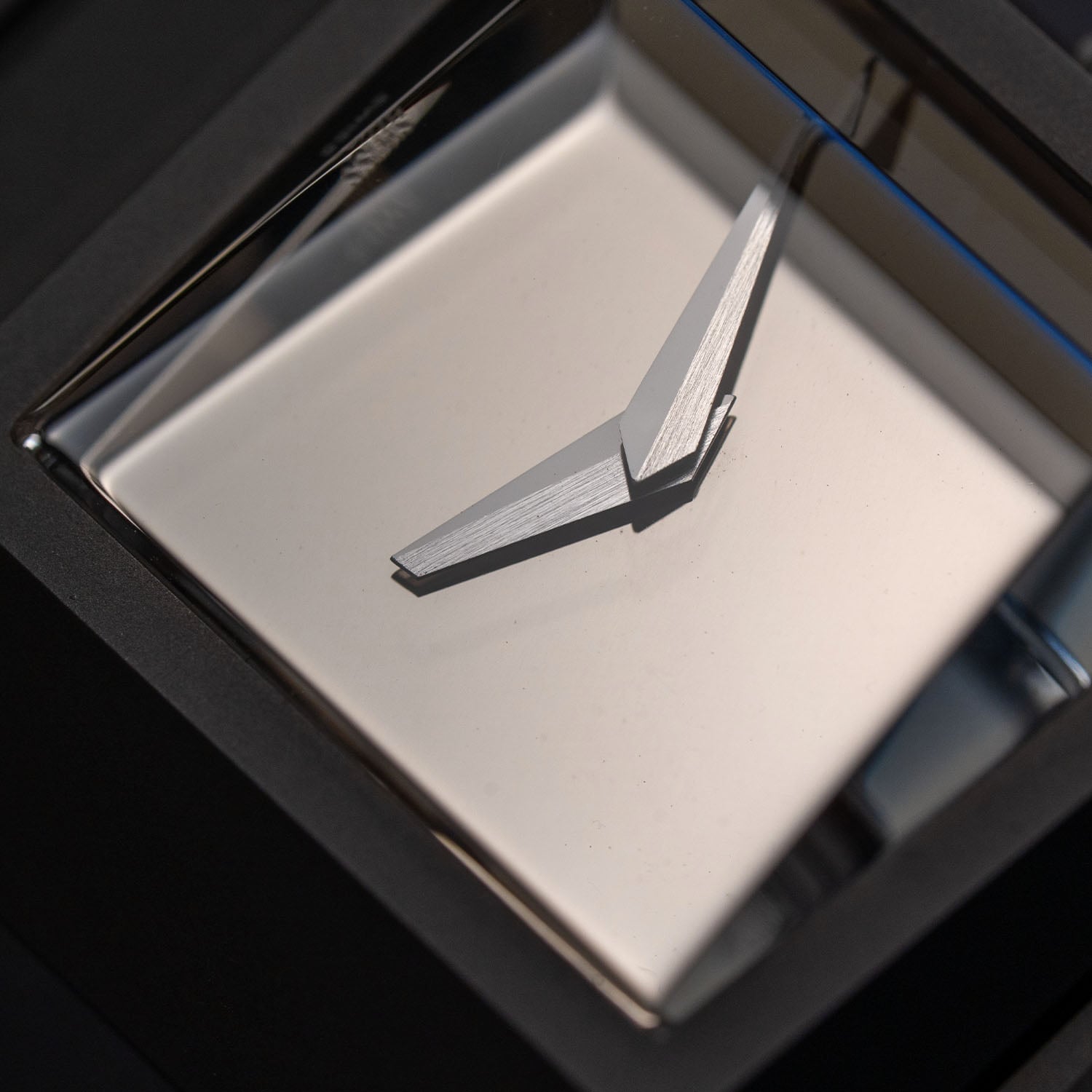 Macro of the two faceted hands, brushed and polished, floating over the unadorned mirror dial of the Toledano & Chan Breutalist