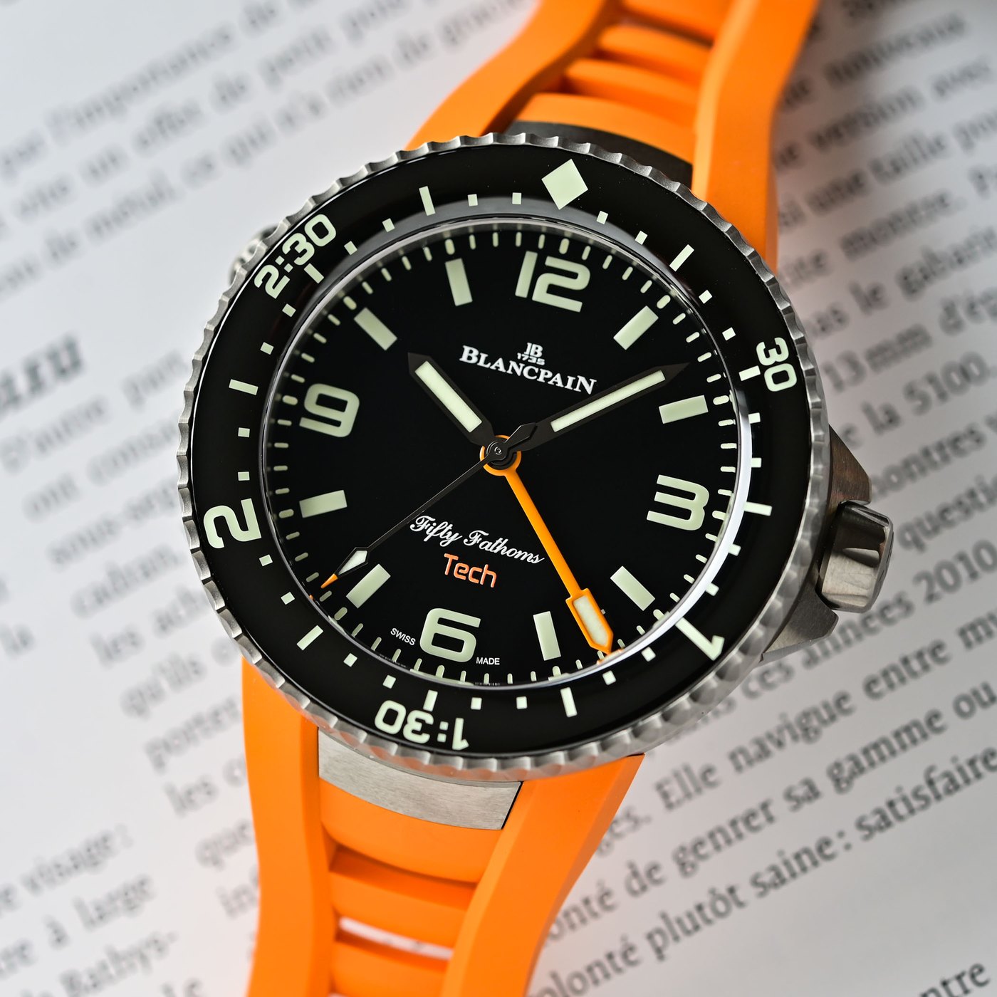 Dial macro of the Blancpain Fifty Fathoms Tech Ref. 5019A, Absolute Black dial with green luminescent markers, orange central three-hour dive hand and Fifty Fathoms Tech text in orange, on an orange rubber strap
