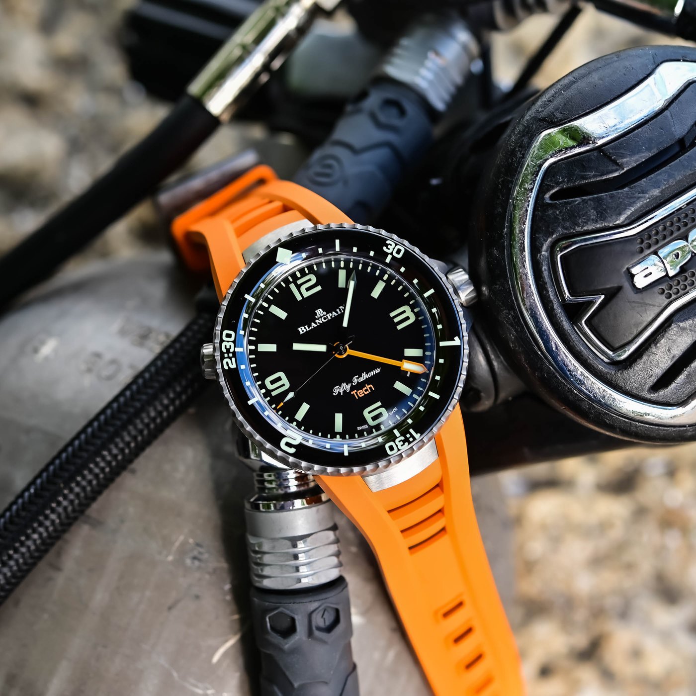 The titanium Fifty Fathoms Tech 5019A photographed at an angle resting against a scuba regulator, showing the case flank, unidirectional three-hour bezel and orange rubber strap