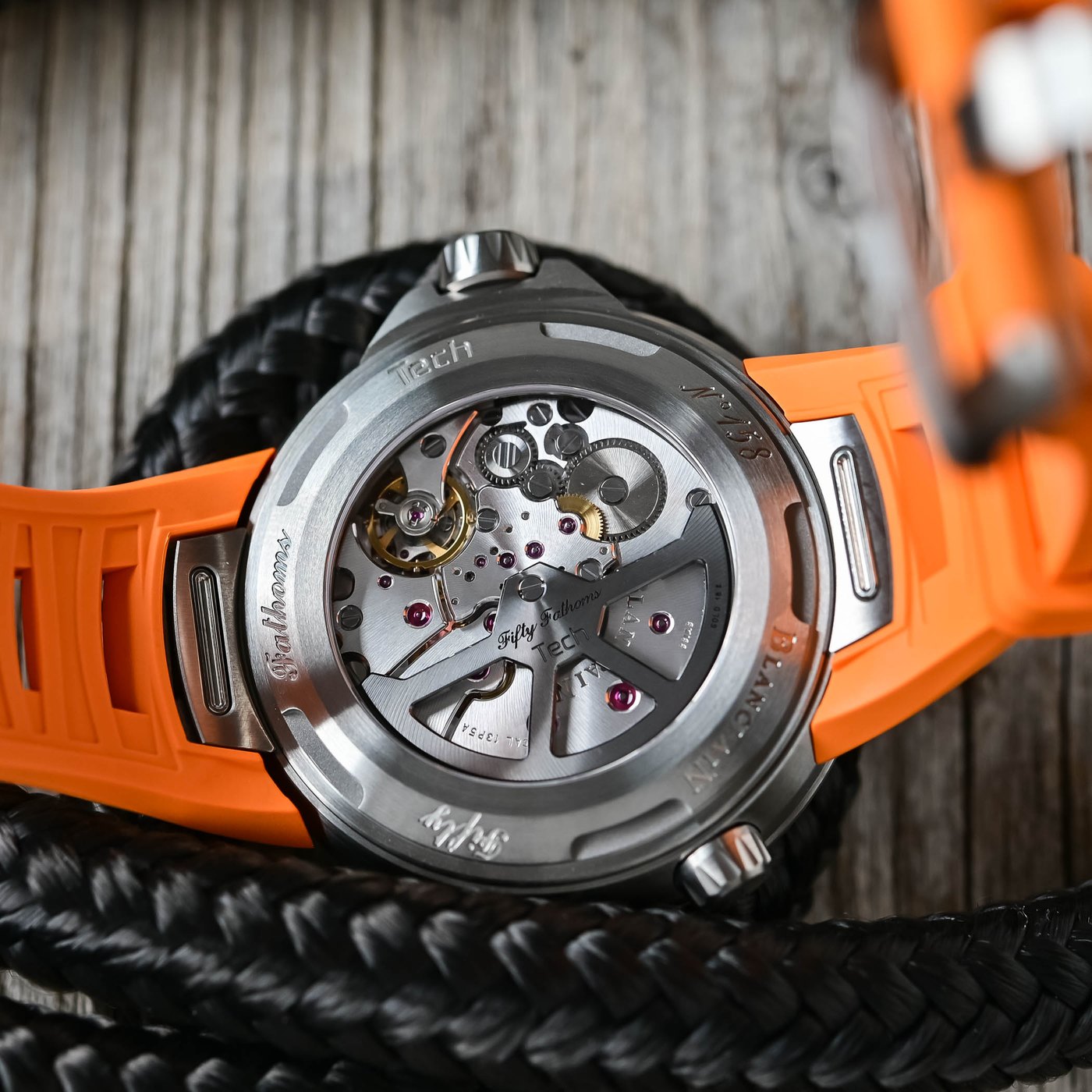 Sapphire caseback of the Fifty Fathoms Tech 5019A showing the automatic Calibre 13P5A, the titanium case and the orange strap, with Fifty Fathoms and Tech engraved on the movement bridges