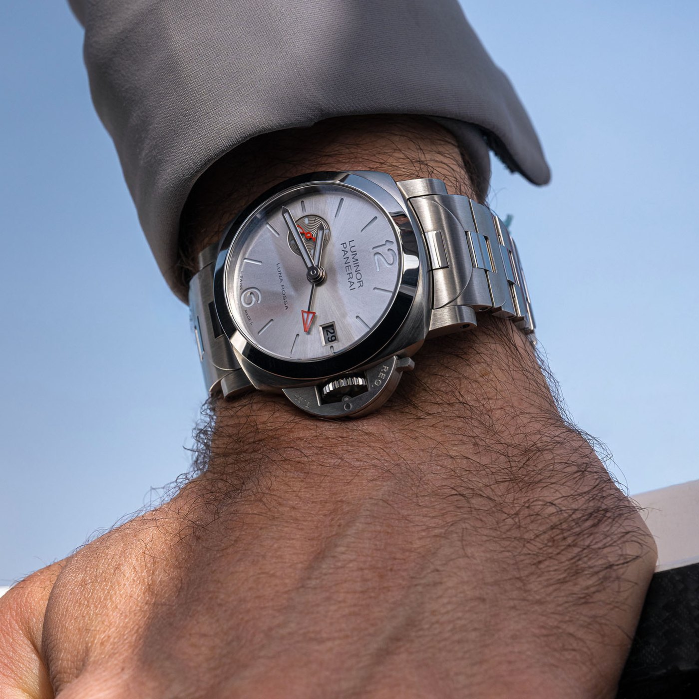 The Luna Rossa GMT PAM01791 on the wrist against a blue sky, steel bracelet and silver dial with the red GMT hand and date visible