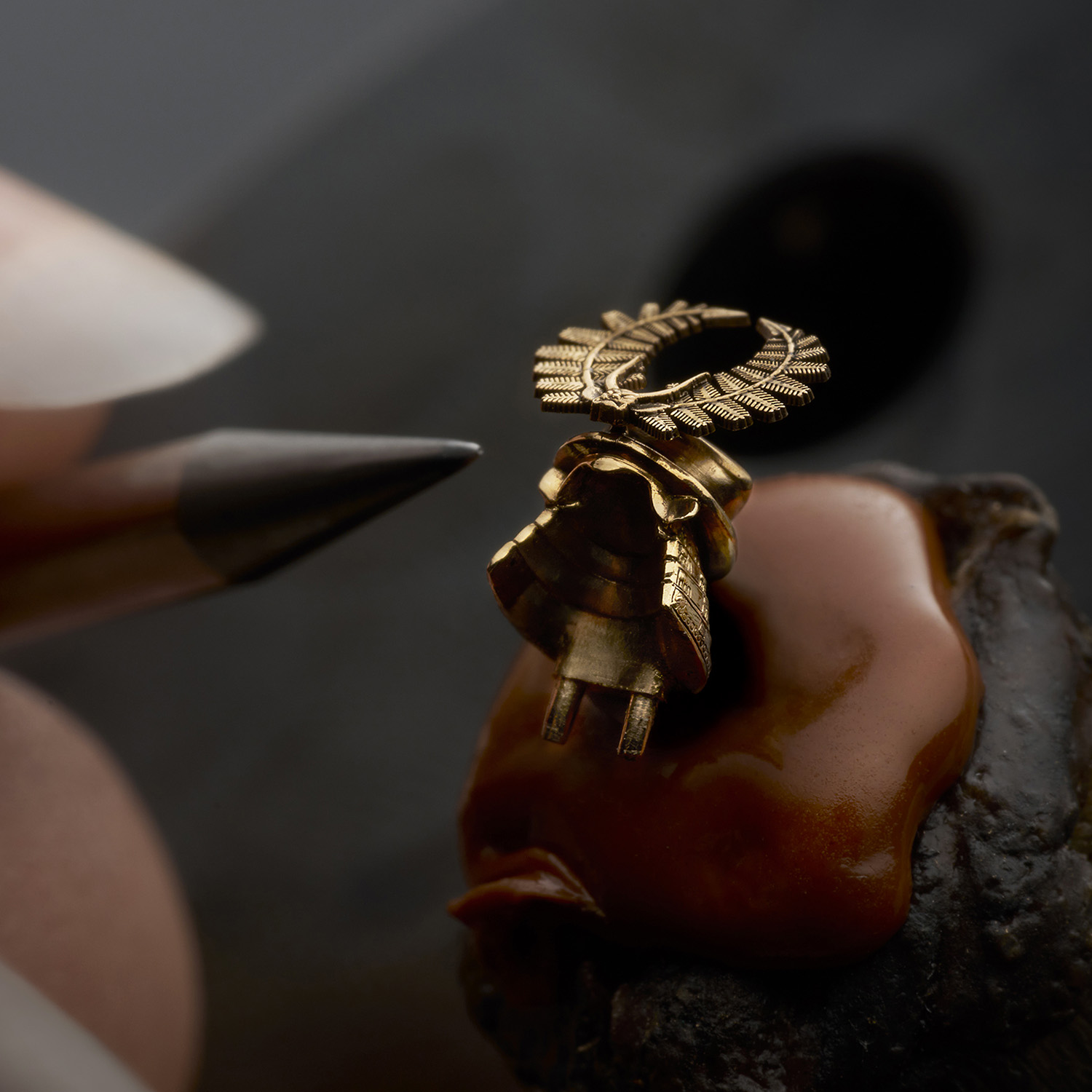 A single 18k pink-gold kabuto helmet held on an engraver's block while its fern crest is finished by hand, showing the depth of the métiers d'art work