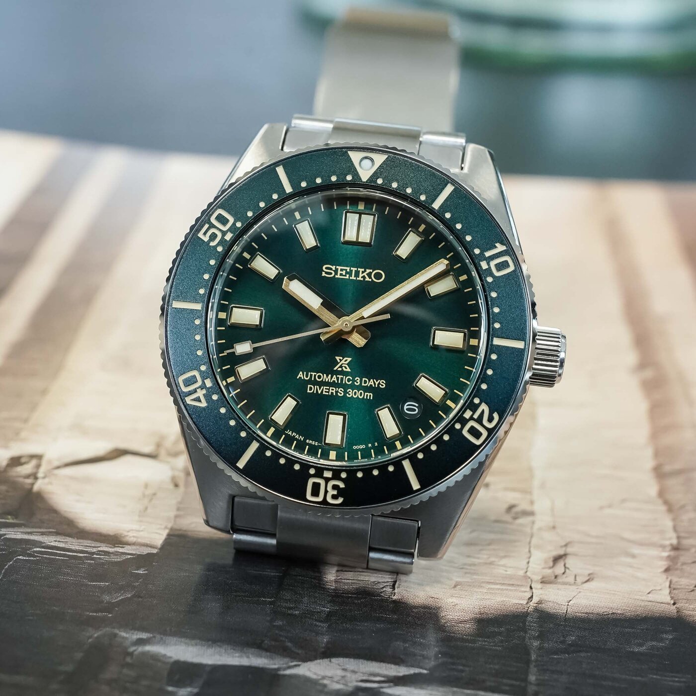 Three-quarter view of the Seiko Prospex 1965 Heritage Diver HBC010 resting on stone, sunray-brushed dark green dial with gilt applied markers and faceted hands, cream Lumibrite, date at 4:30 and Automatic 3 Days Diver's 300m text, dark green coin-edge bezel on the three-link steel bracelet