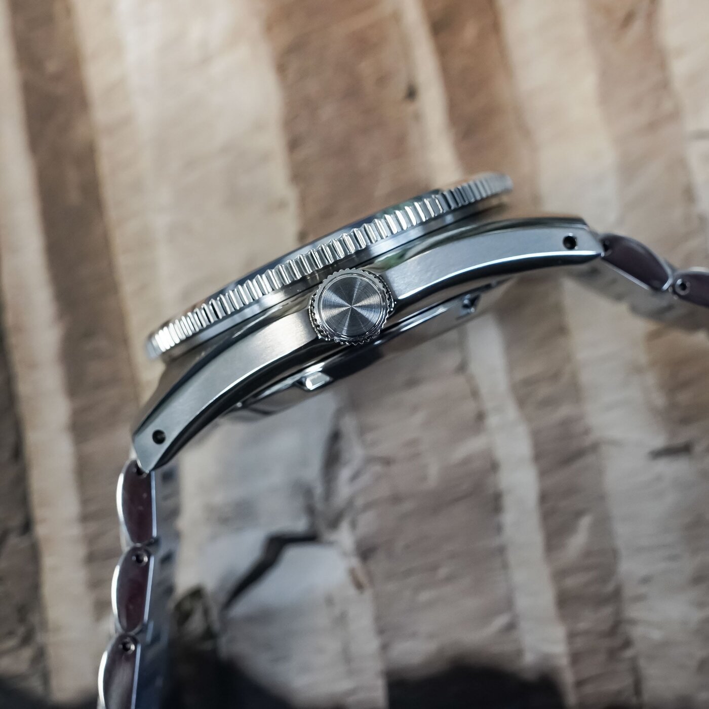 Side profile of the HBC010 showing the coin-edge dark green bezel, the screw-down crown and the brushed steel case flank, on the three-link steel bracelet