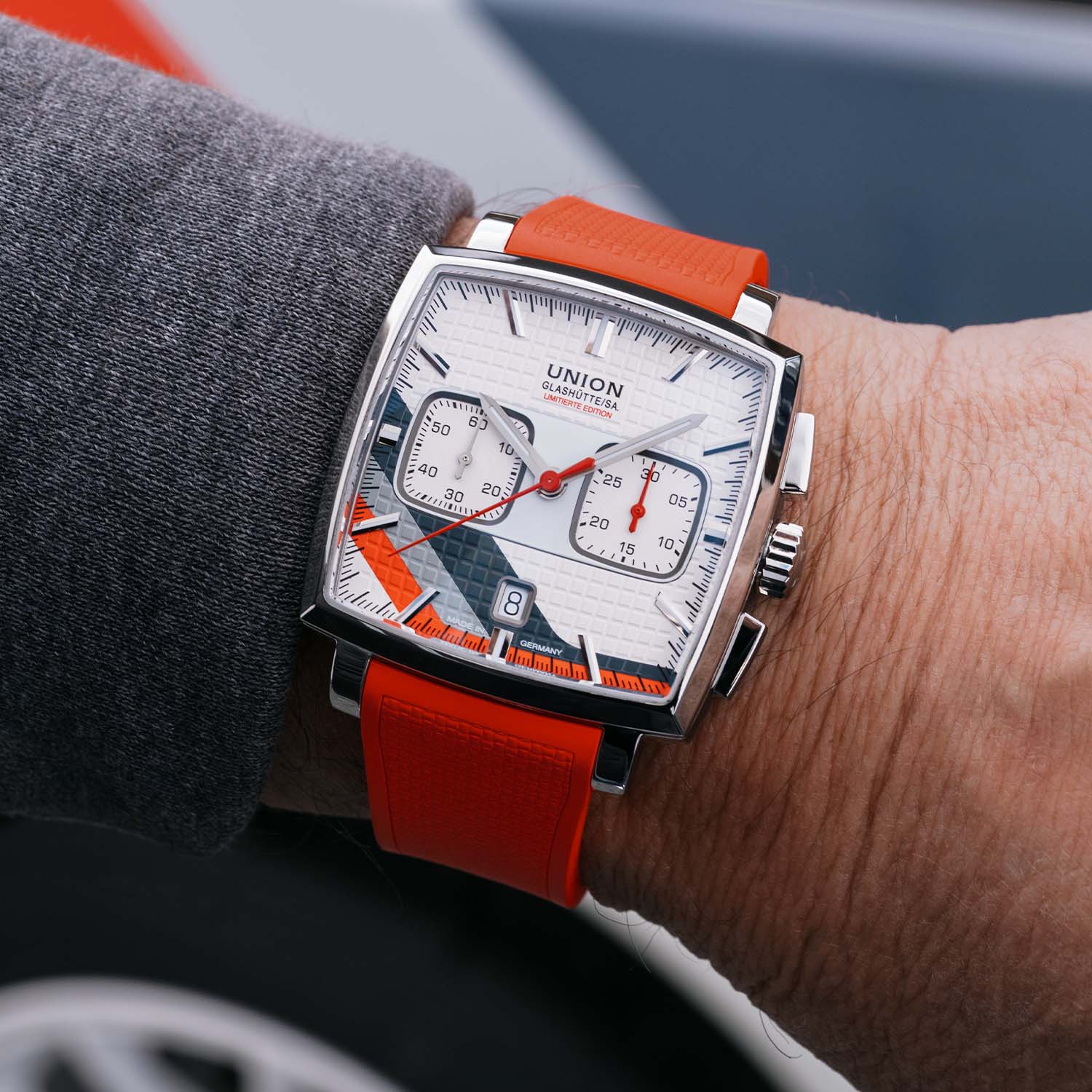The square Union Glashütte Averin Sachsen Classic 2026 worn on the wrist on its bright red rubber strap, showing the crown between two rectangular chronograph pushers